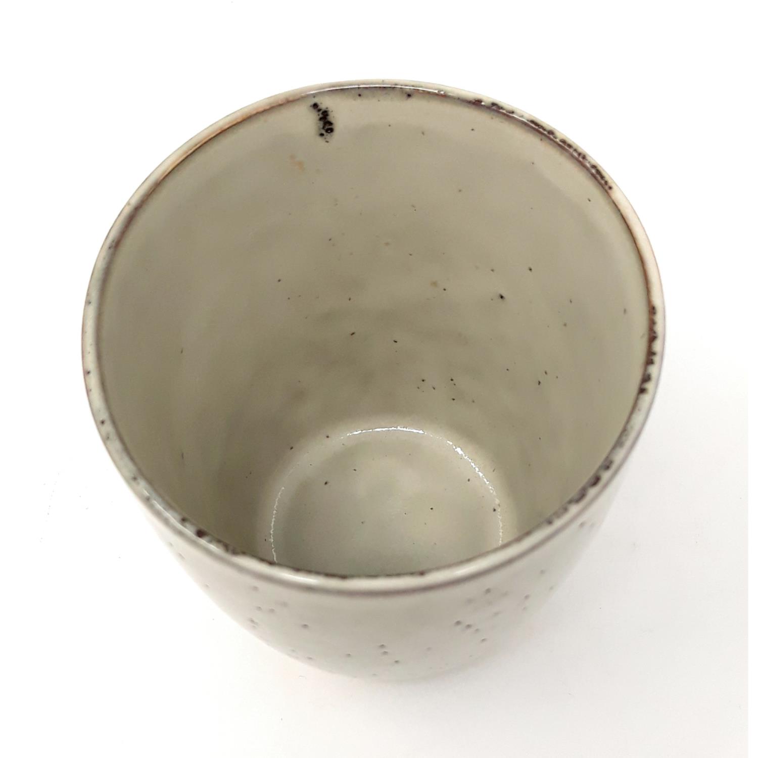 Ein grauer, glatter Becher aus Keramik, innen hohl, mit leicht unregelmäßiger Oberfläche und kleinen Punkten.