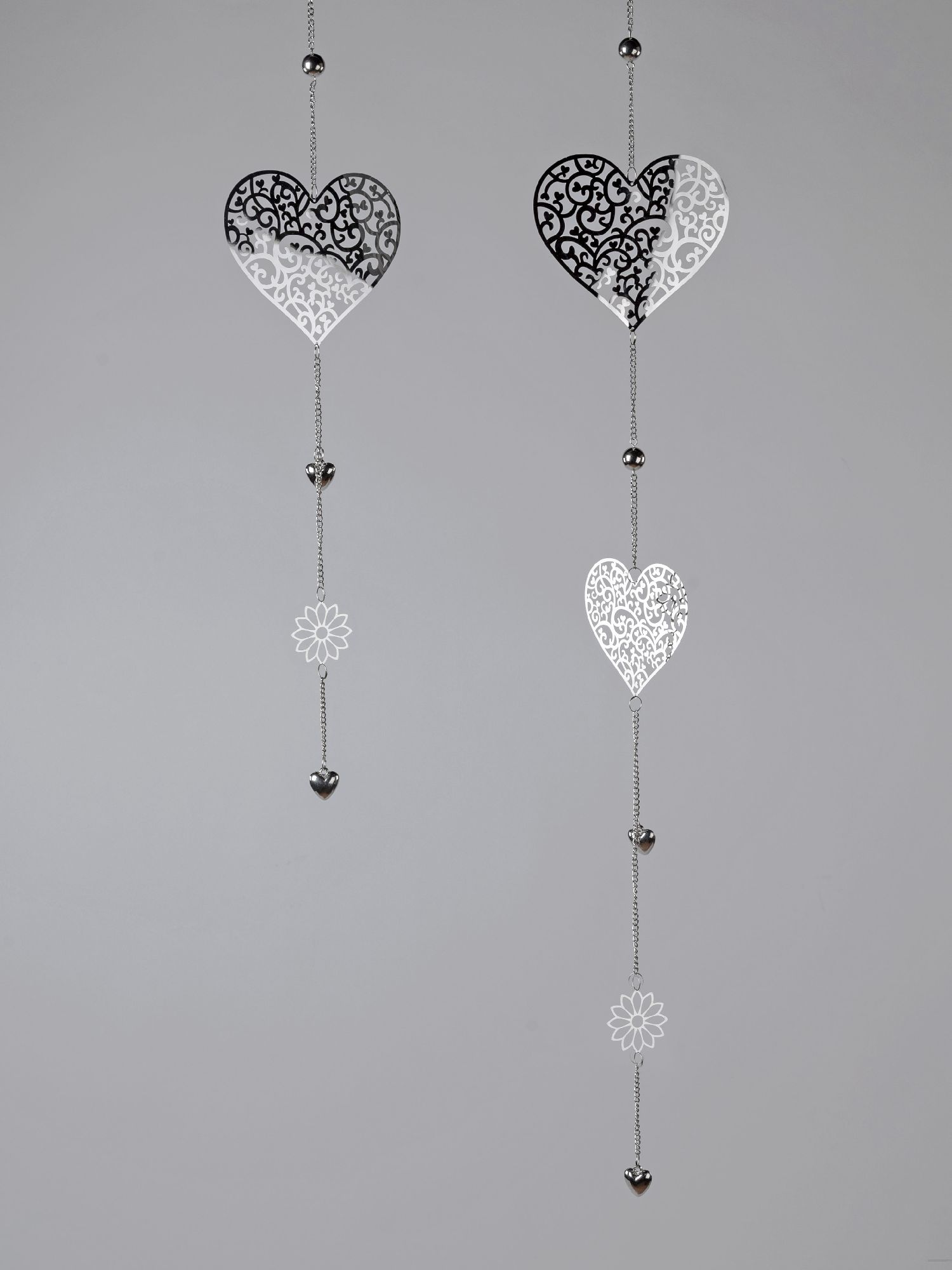 Zwei hängende Herzen in Schwarz und Weiß mit filigranen Mustern, verbunden durch Ketten mit kleinen Blüten und Herzen.