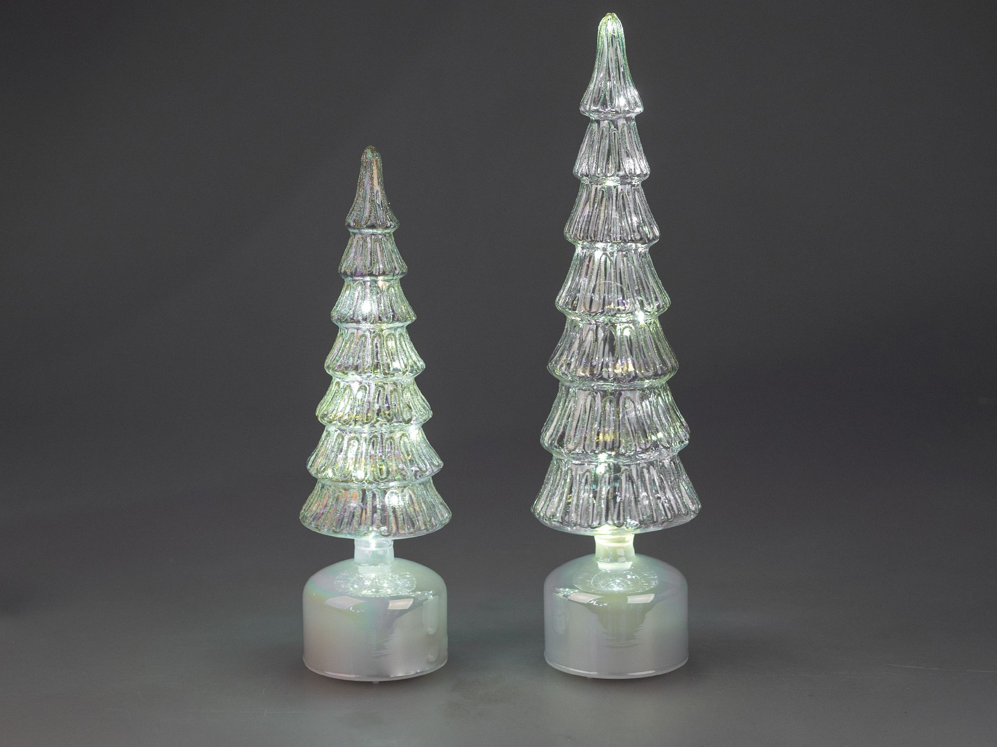 Zwei durchsichtige, glitzernde Weihnachtsbäume aus Glas, einer größer als der andere, auf runden, we