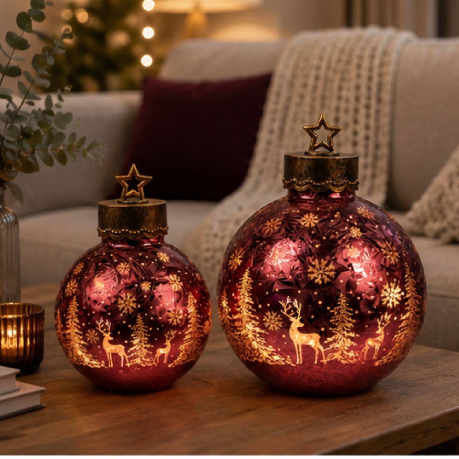 Zwei leuchtende rote Kugellampen mit Rentier- und Tannenmotiven auf Holztisch im Wohnzimmer