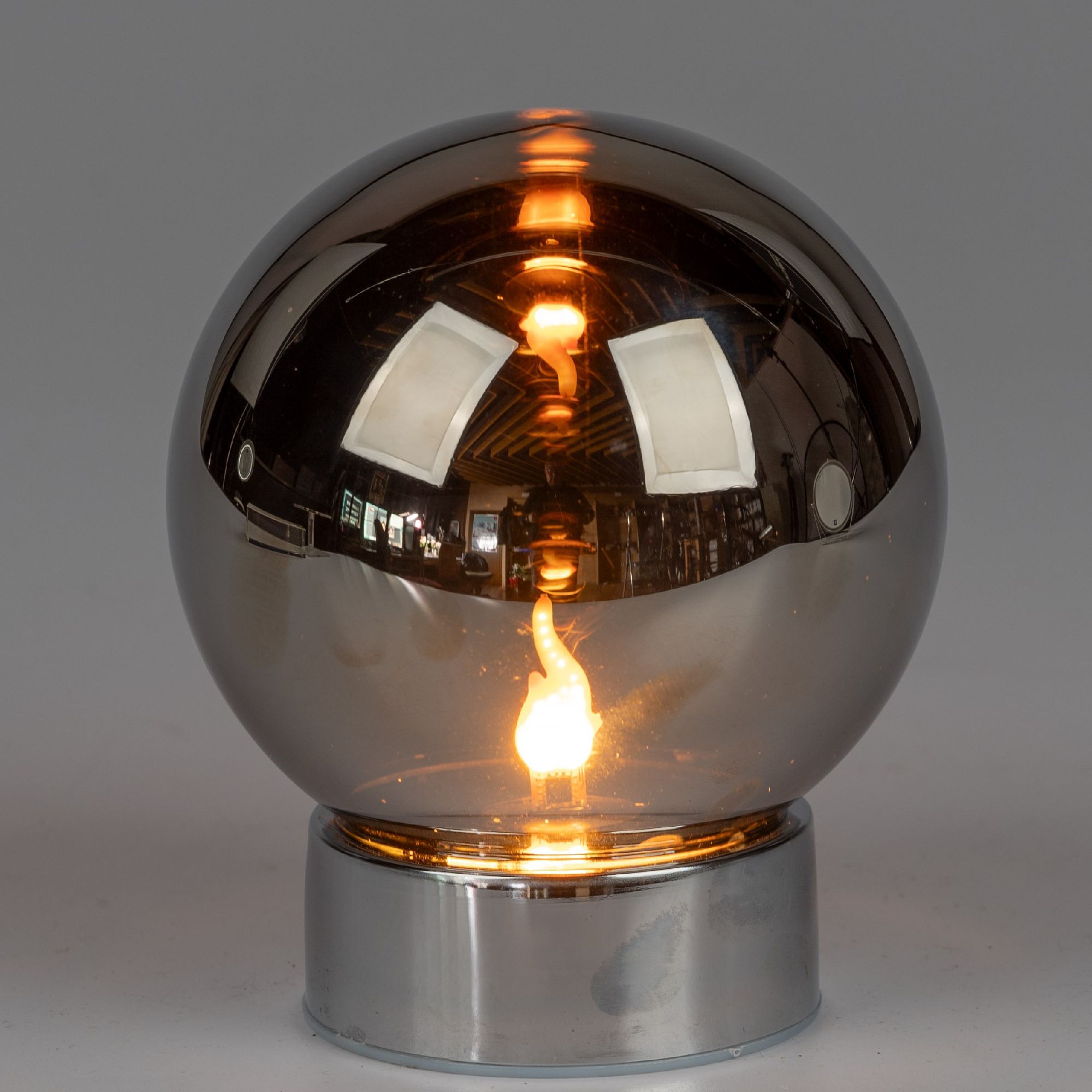 Runde Lampe mit reflektierender, bronzefarbener Oberfläche und leuchtender Glühbirne im Inneren.