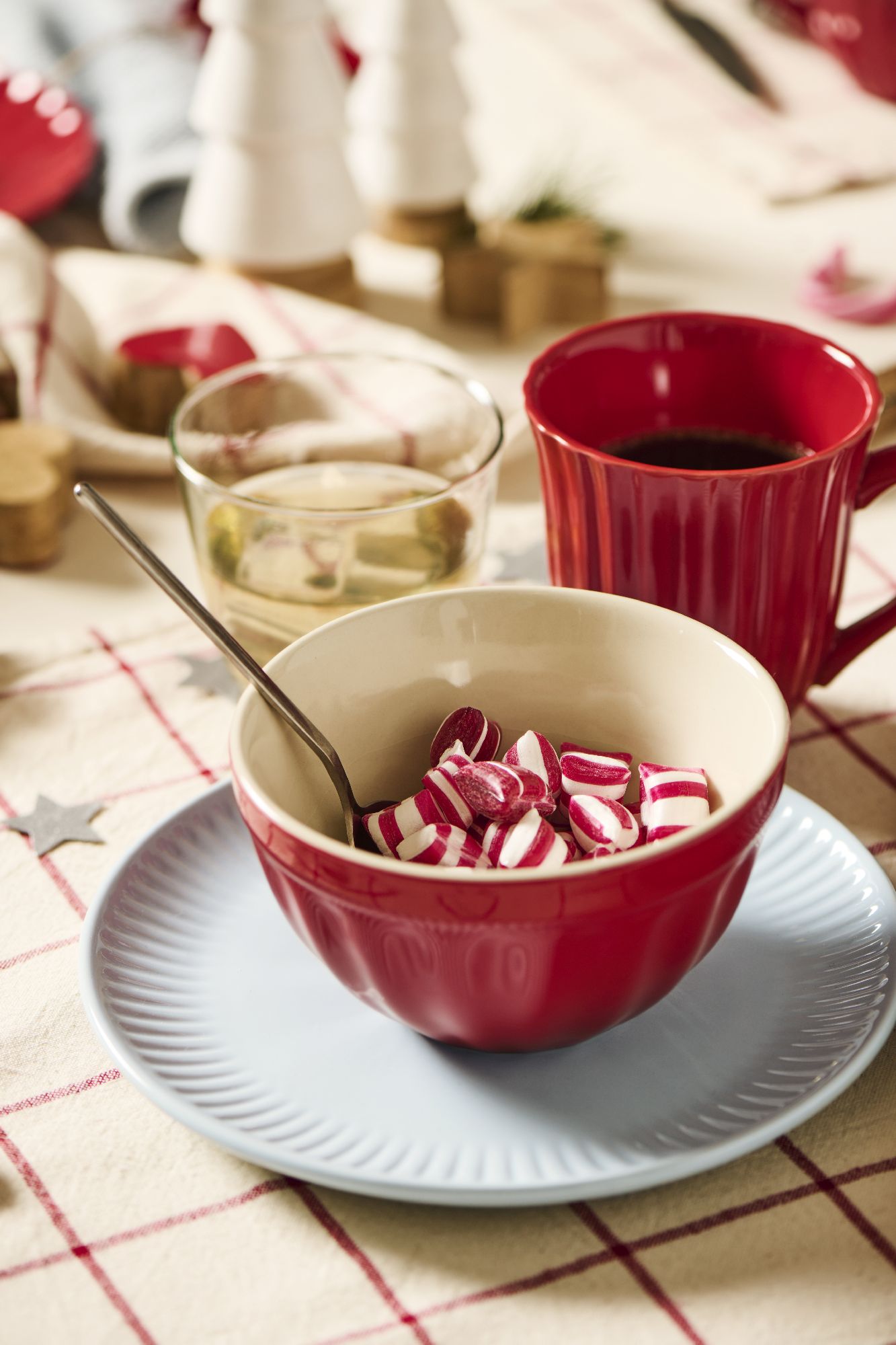 Eine rote Schüssel mit gestreiften Bonbons steht auf einem blauen Teller. Daneben sind Gläser und eine Tasse zu sehen.