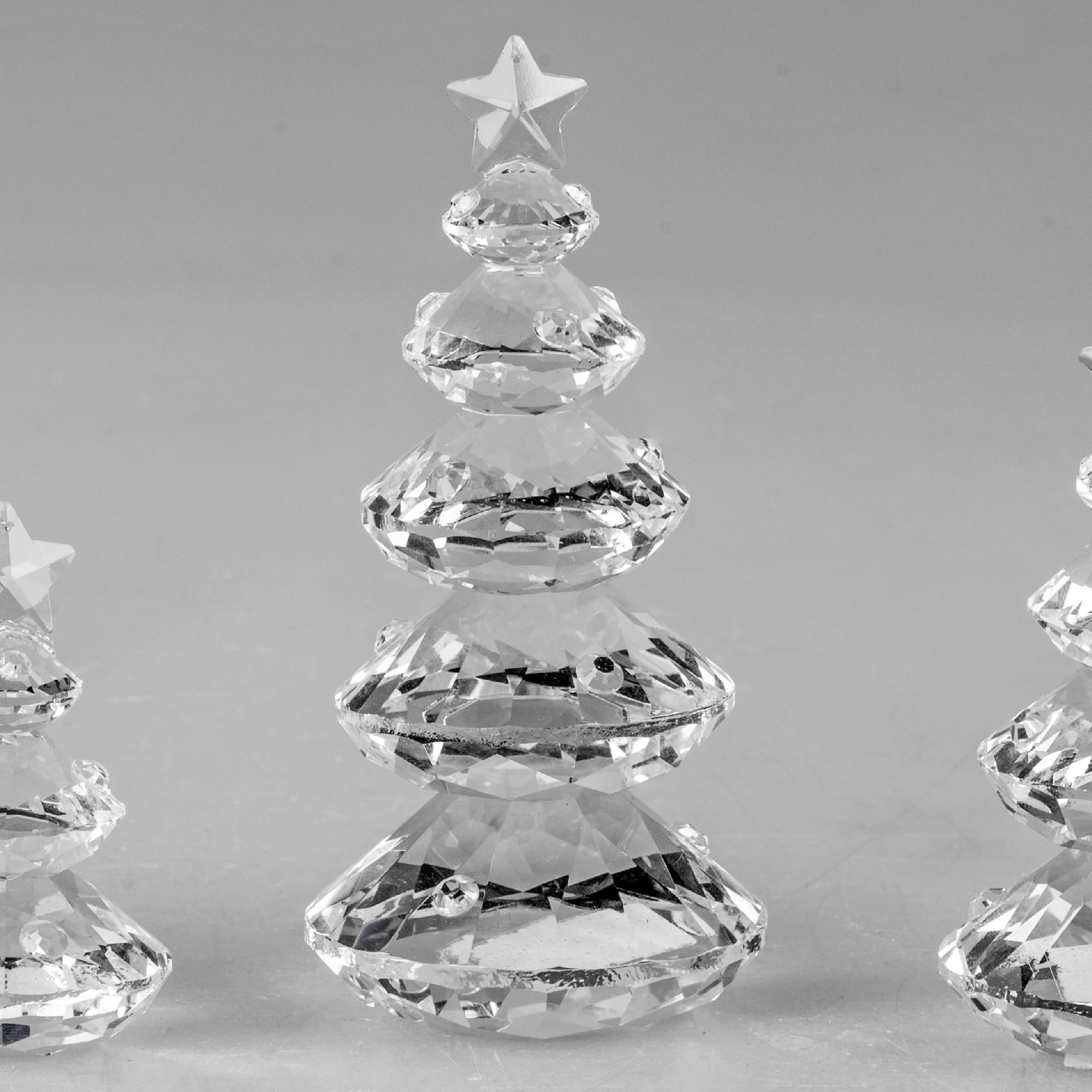 Drei gläserne Weihnachtsbäume in verschiedenen Größen, mit einer Sternspitze, auf einem grauen Hinte