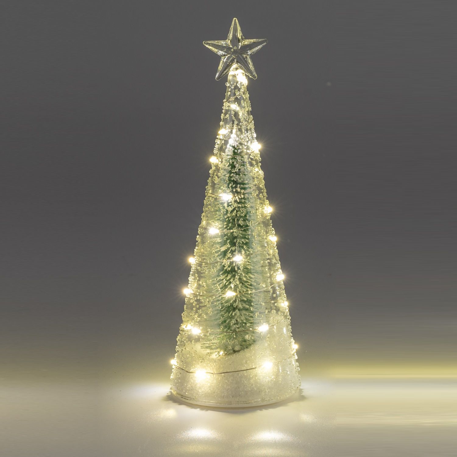 Ein dekorativer Weihnachtsbaum aus Glas mit einer Spitze in Sternform und warmen Lichtern, auf einem