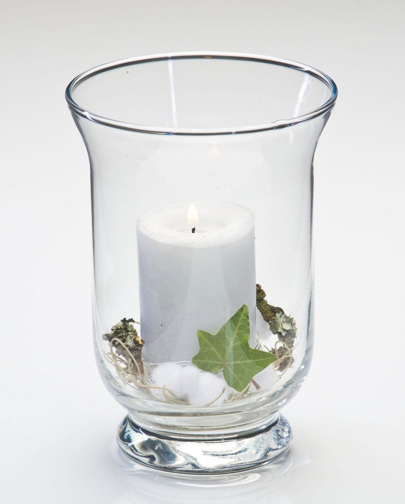 Ein transparentes Glasgefäß mit einer brennenden weißen Kerze, umgeben von Moos, Baumwolle und einem grünen Blatt.