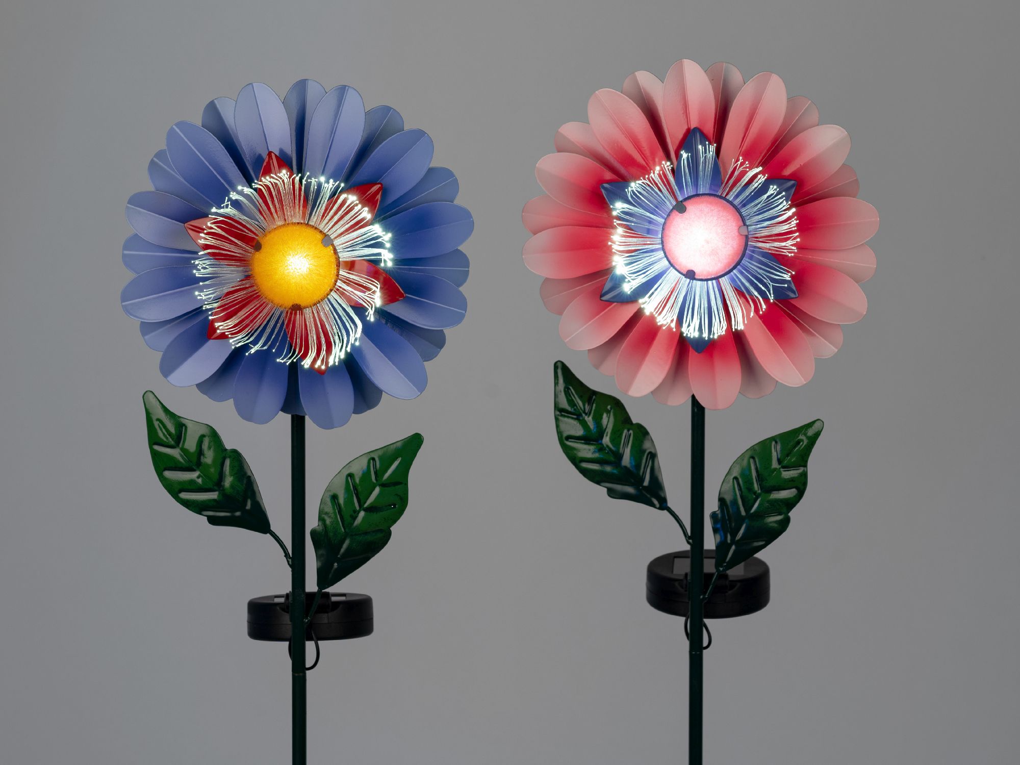 Zwei bunte Blumen aus Kunststoff, eine blau und eine rot, mit leuchtenden Mittelteilen und grünen Blättern, vor grauem Hintergrund.