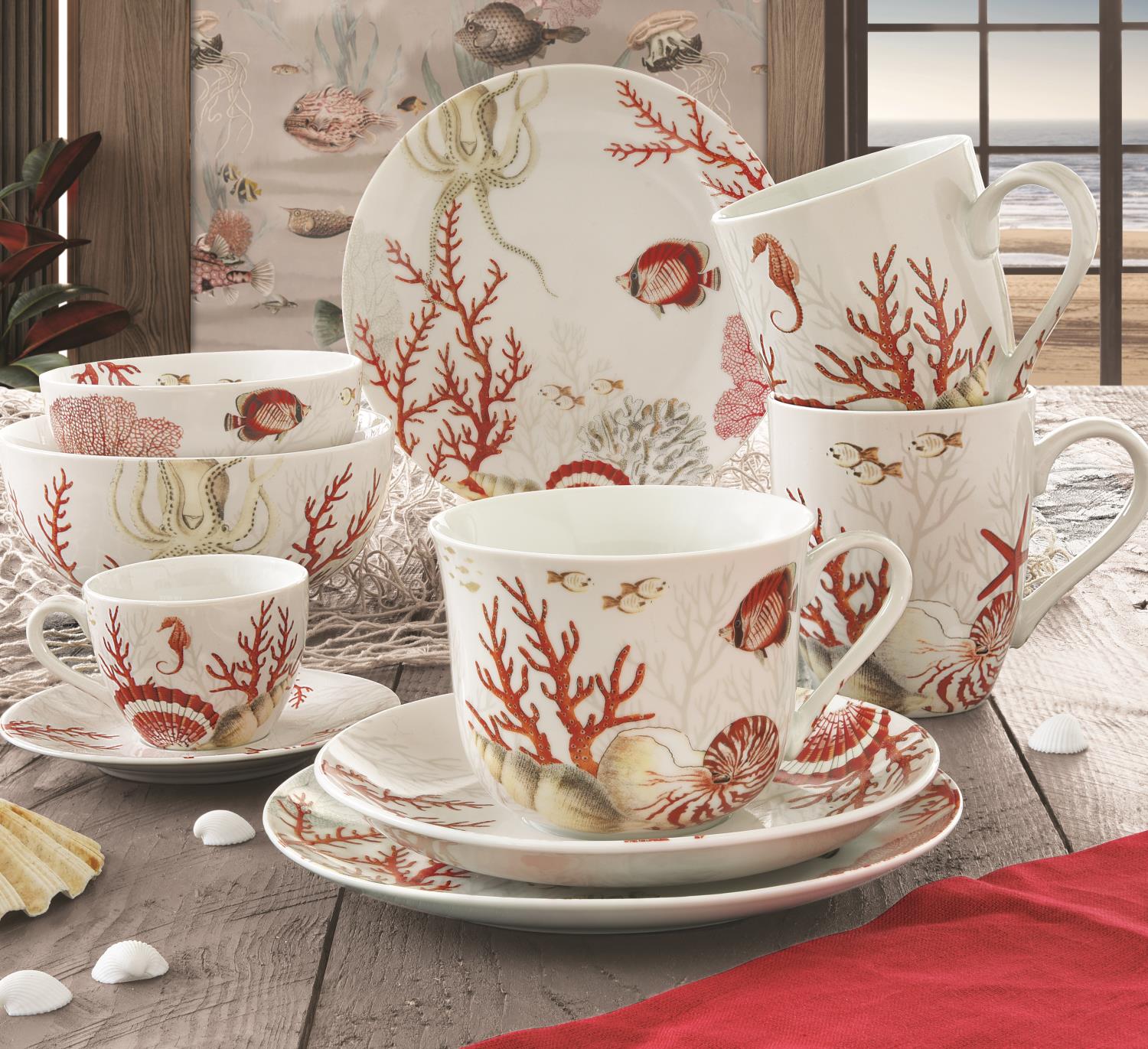 Ein Set aus Geschirr mit roten Korallen- und Meeresmotiven, bestehend aus Tassen, Tellern und Schalen auf einem Holztisch.