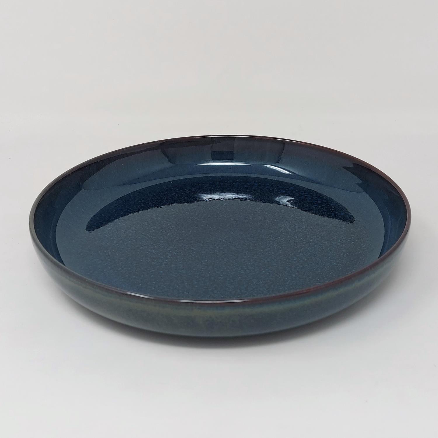 Ein flacher, runder Teller in dunklem Blau mit glatter Oberfläche und leicht gewölbtem Rand.