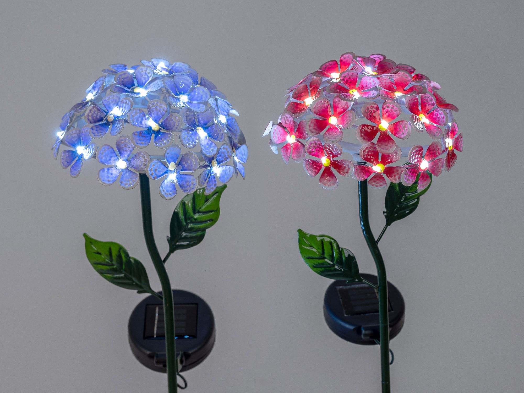 Zwei solarbetriebene Blumenleuchten, eine in Blau und eine in Rot, mit leuchtenden Blüten und grünen