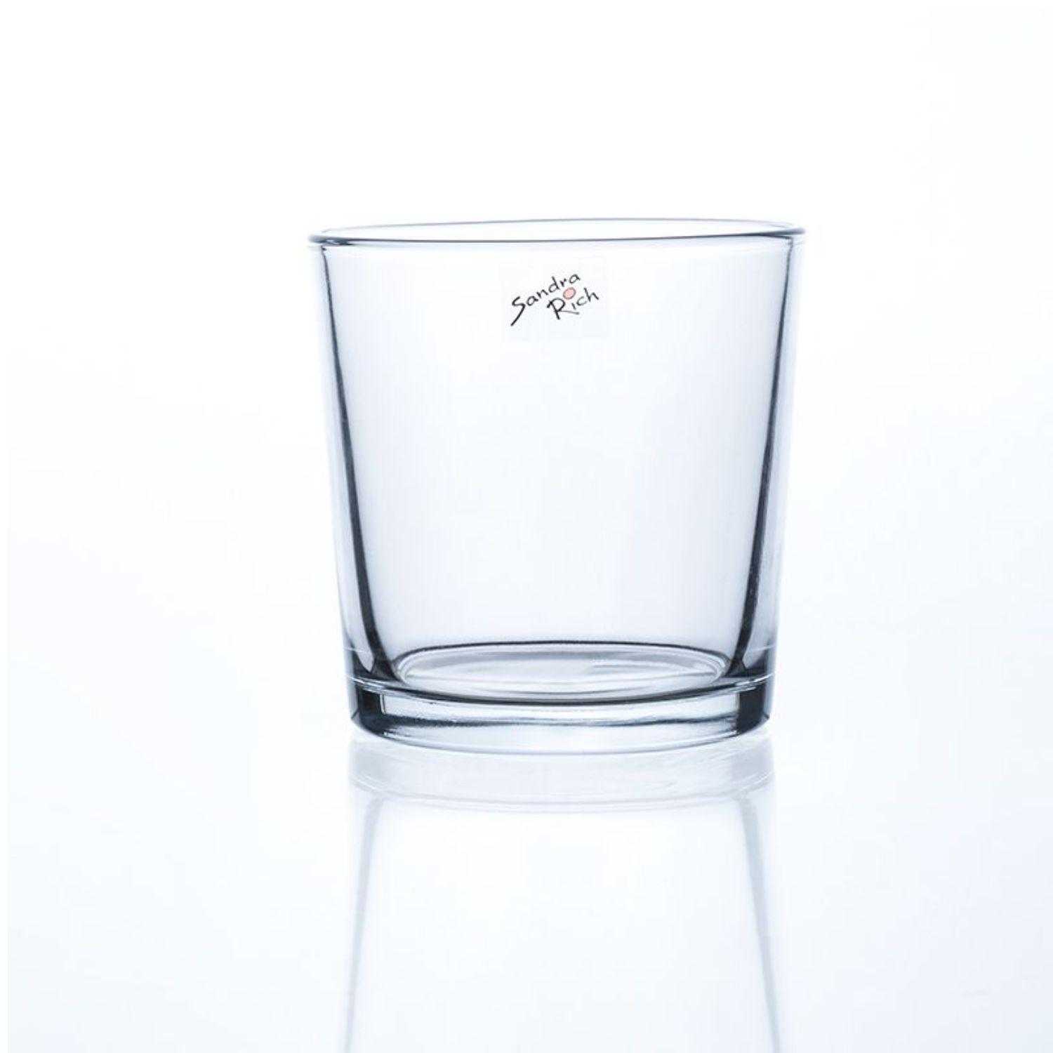 Ein transparenter Glasbecher mit geradem Rand und einem flachen Boden. Auf der Oberfläche ist ein kleiner Aufkleber sichtbar.