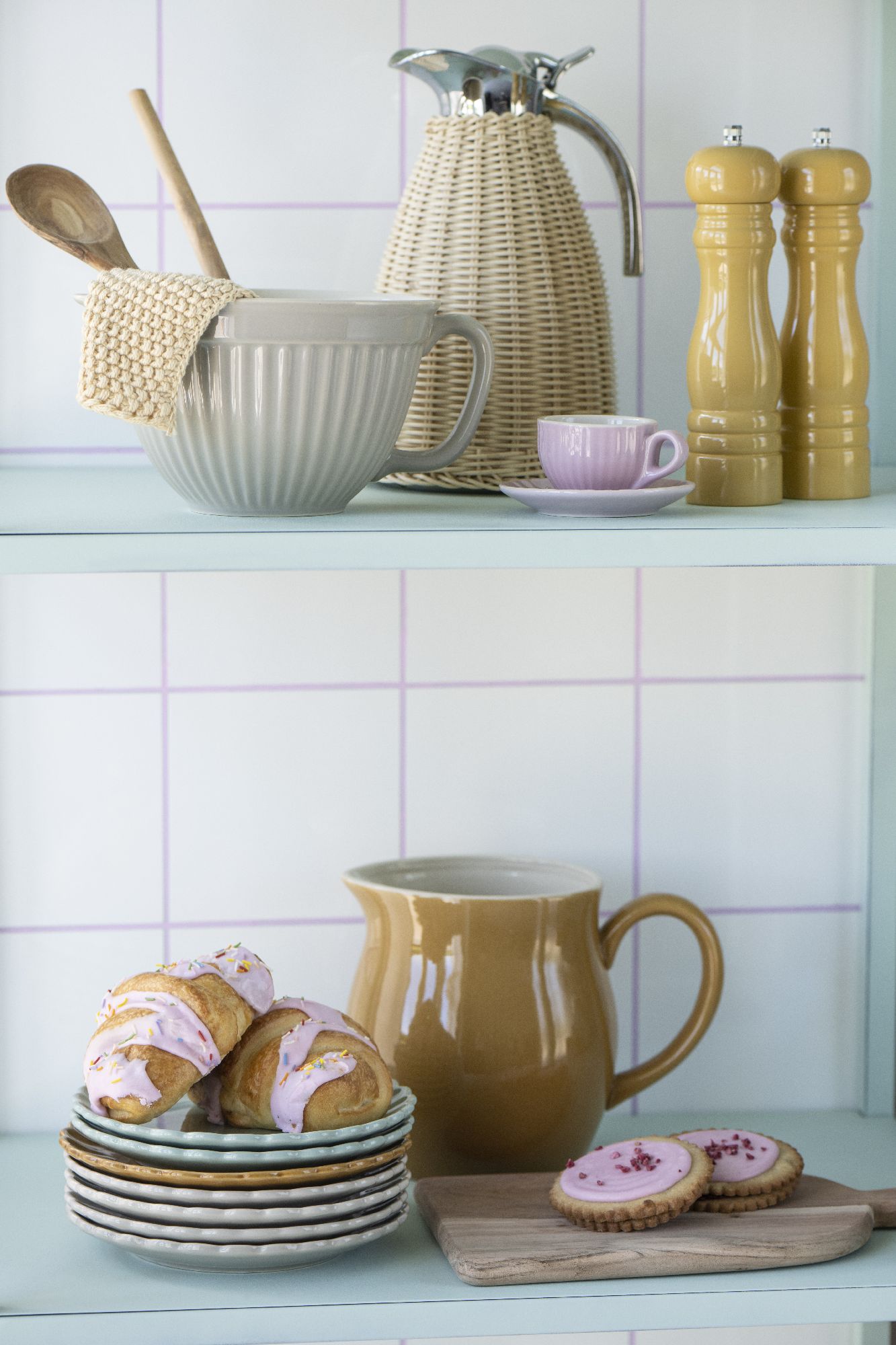 Auf einem Regal stehen eine Schüssel, eine Kanne, Gewürzmühlen, Teller mit Gebäck und eine Tasse.