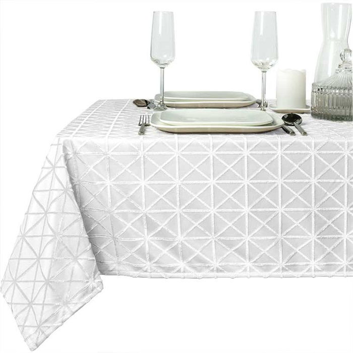 Tisch mit weißer, gemusterter Tischdecke, zwei Gläsern, Tellern, Besteck und einer Kerze auf einem Tisch.