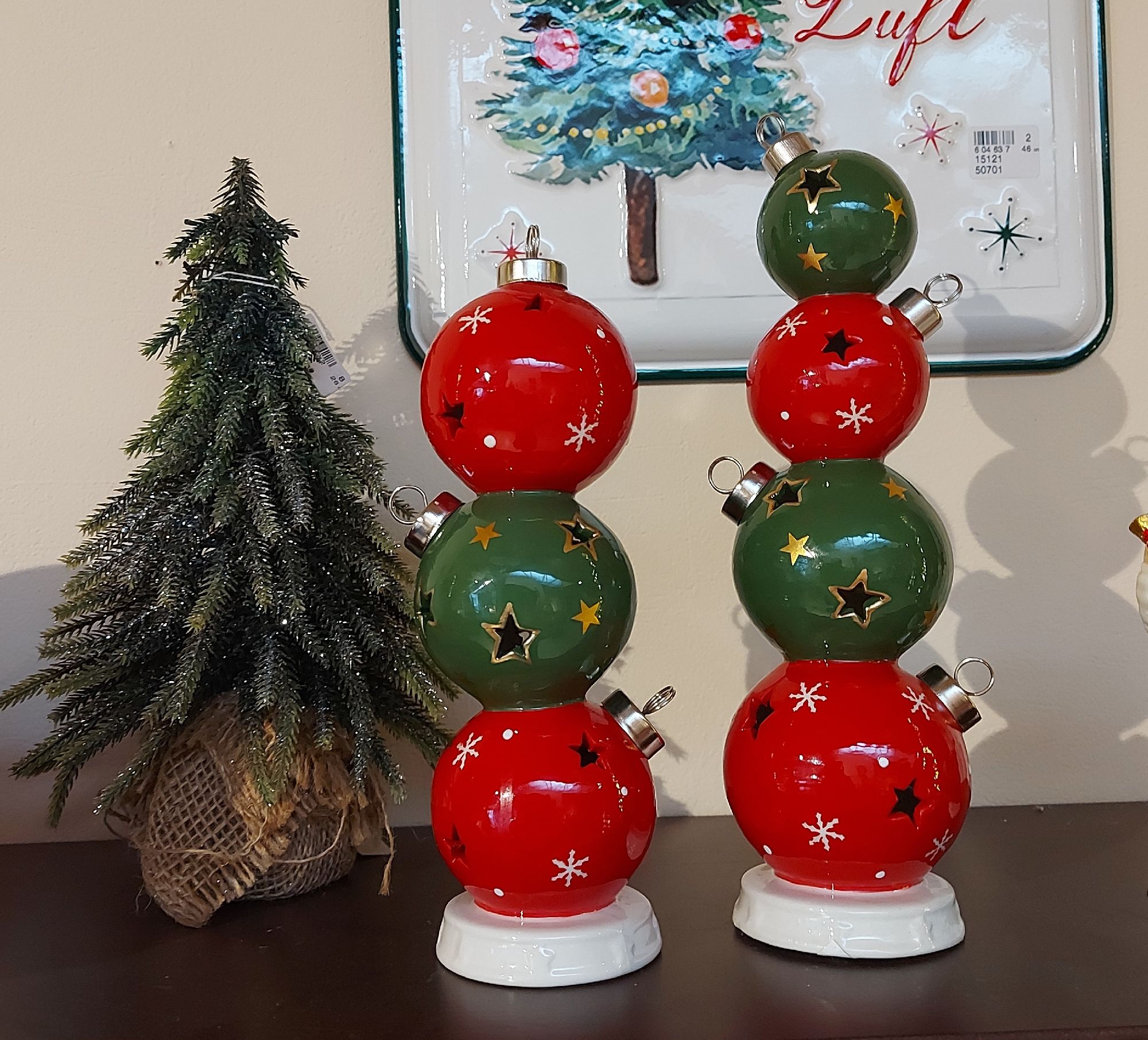 Zwei dekorative Figuren aus roten und grünen Kugeln stehen neben einem kleinen Weihnachtsbaum auf ei