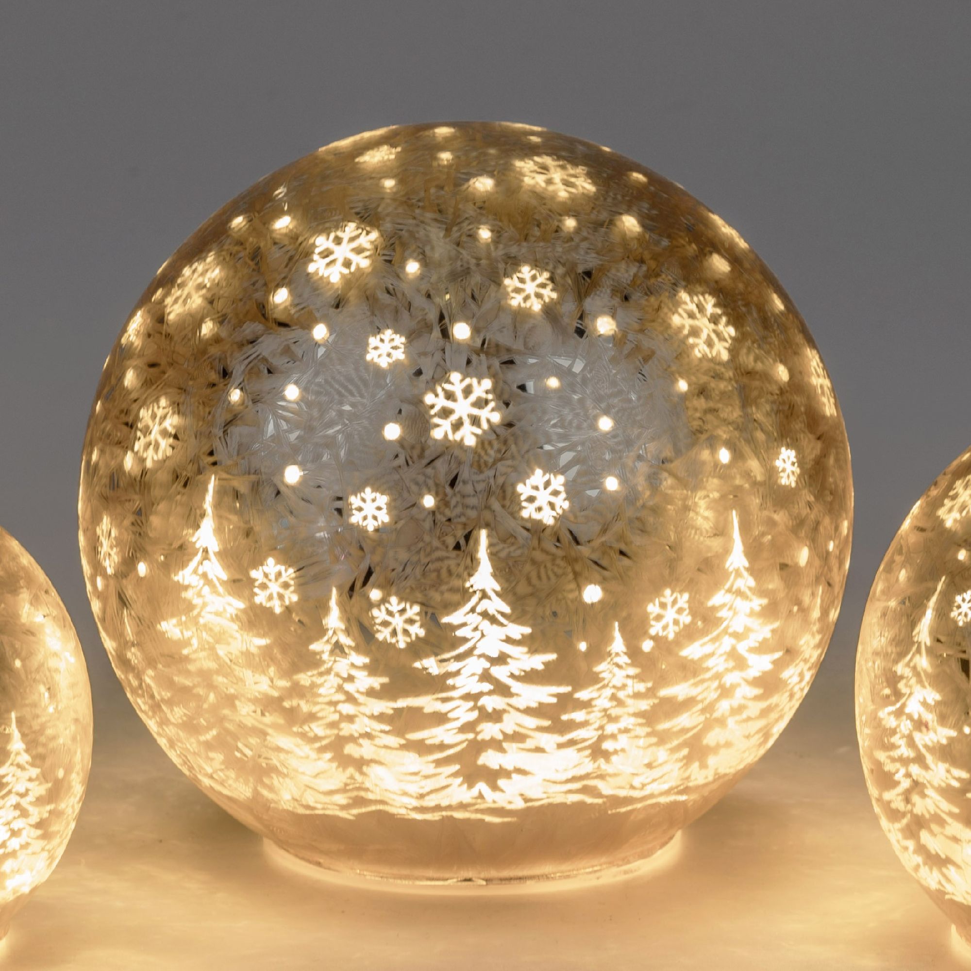 Eine beleuchtete Glaskugel mit Schneeflocken- und Tannenbaum-Motiven, die sanft leuchtet. Im Hinterg