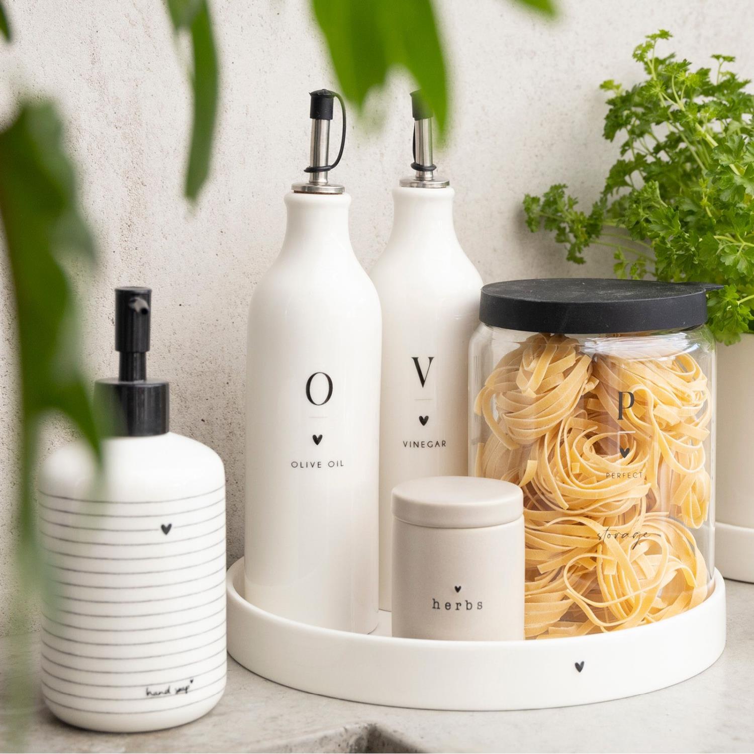 Weiße Flaschen für Olivenöl und Essig, ein Glas mit Teigwaren und ein Behälter für Kräuter auf einem