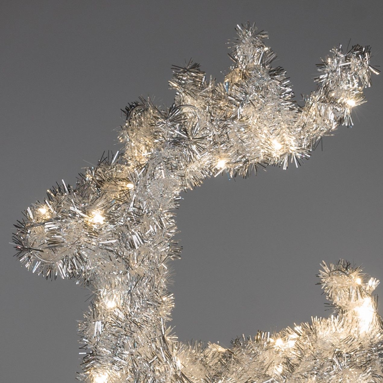 Silberne Weihnachtsdekoration in Form eines Rentiers mit Lichtern, vor einem grauen Hintergrund.