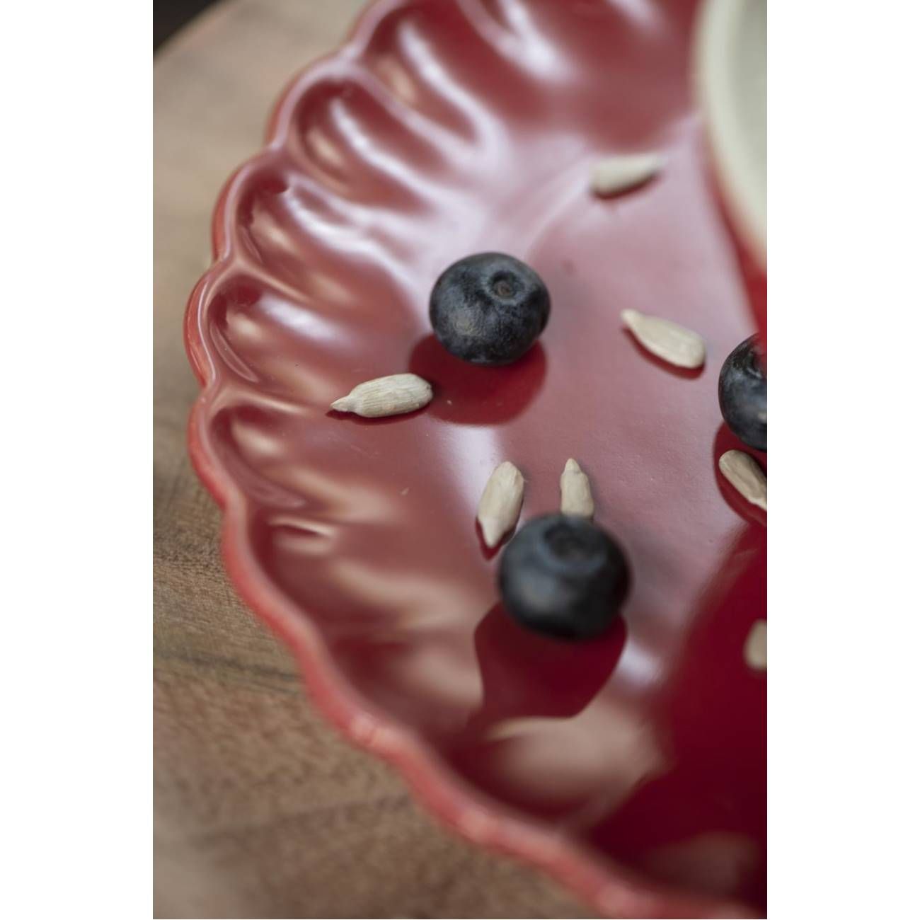 Rote, gewellte Schale mit blauen Heidelbeeren und einigen Sonnenblumenkernen auf einer Holzoberfläche.
