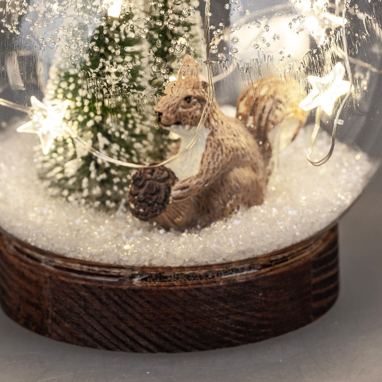 Eine Schneekugel mit einem Eichhörnchen, das eine Tannenzapfen hält, und einem kleinen Weihnachtsbau