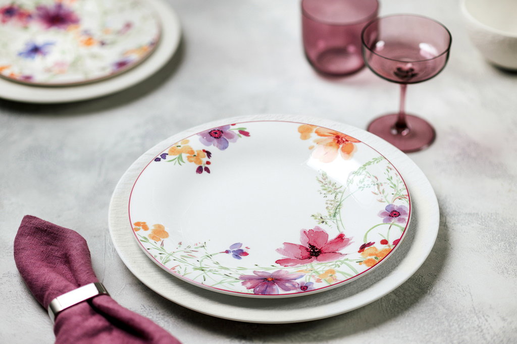 Ein gedeckter Tisch mit einem blumendekorierten Teller, einem Stoffserviette in Lila und verschieden