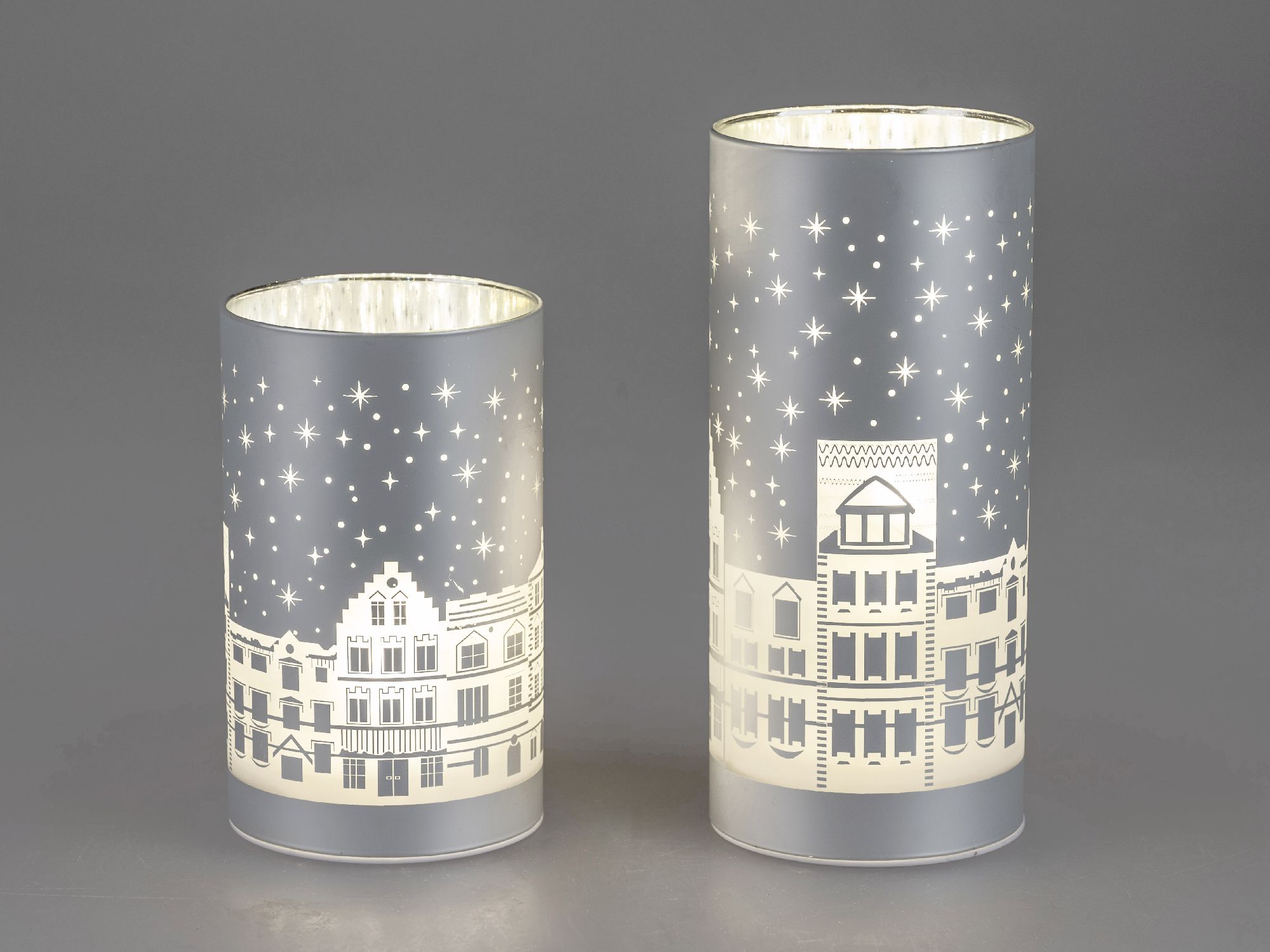 Zwei dekorative Laternen in verschiedenen Höhen, mit durchscheinenden Motiven von Häusern und Sterne