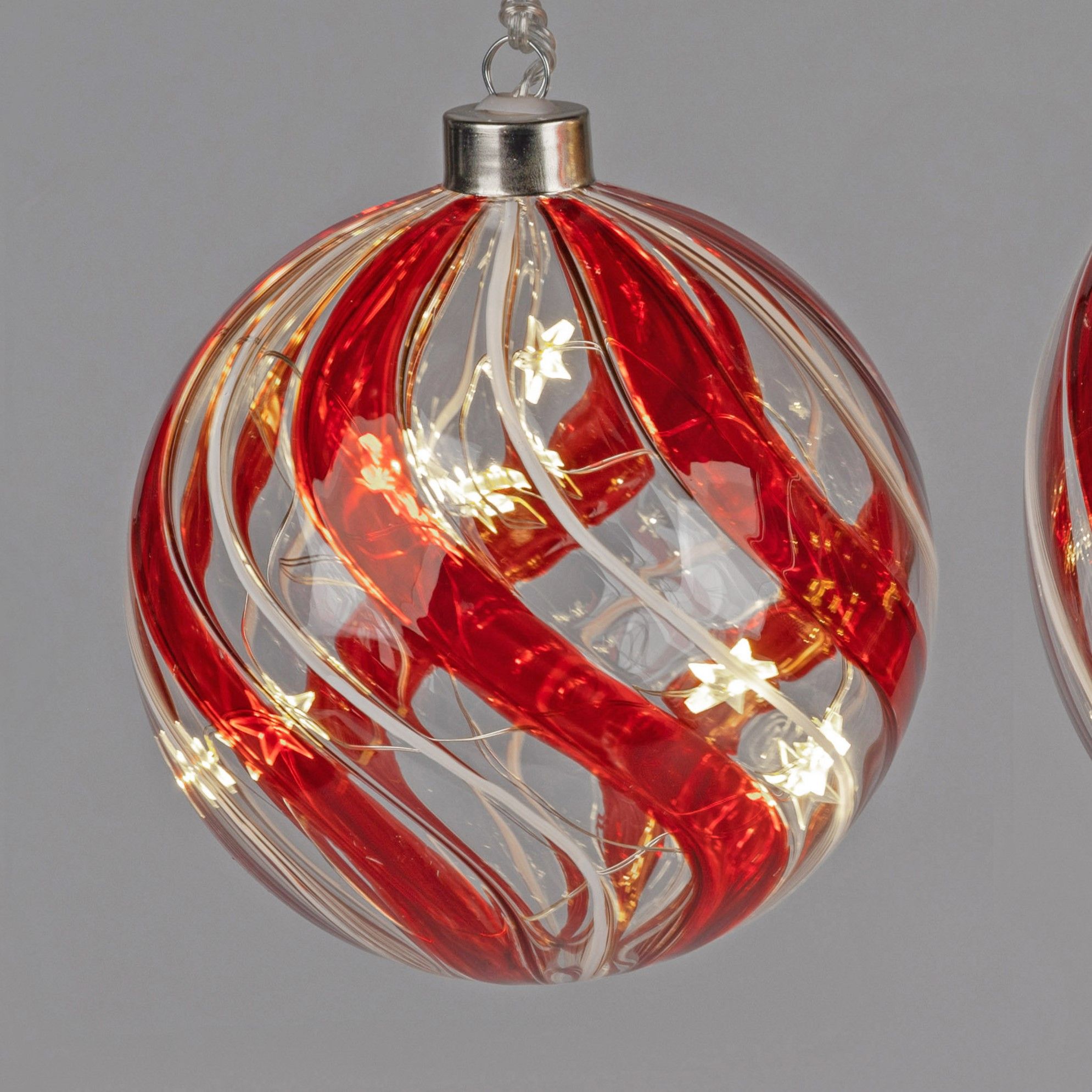 Glänzende Weihnachtskugel in Rot und Transparent mit spiralförmigen Mustern und kleinen Lichtern im