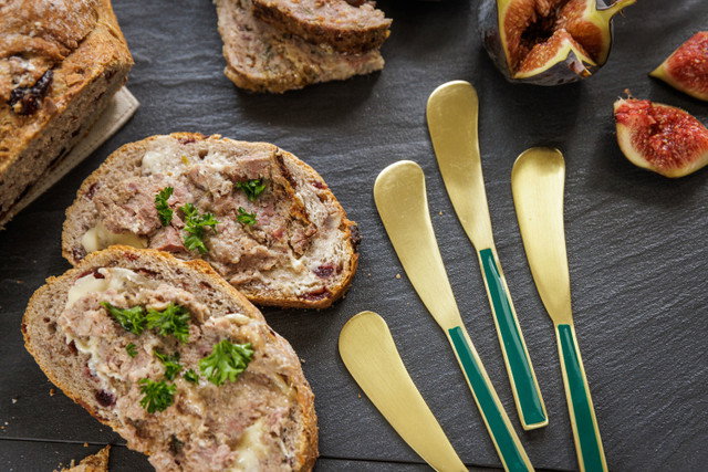 Auf einem schwarzen Untergrund liegen Brotscheiben mit Aufstrich, frische Feigen und goldene Besteckteile.