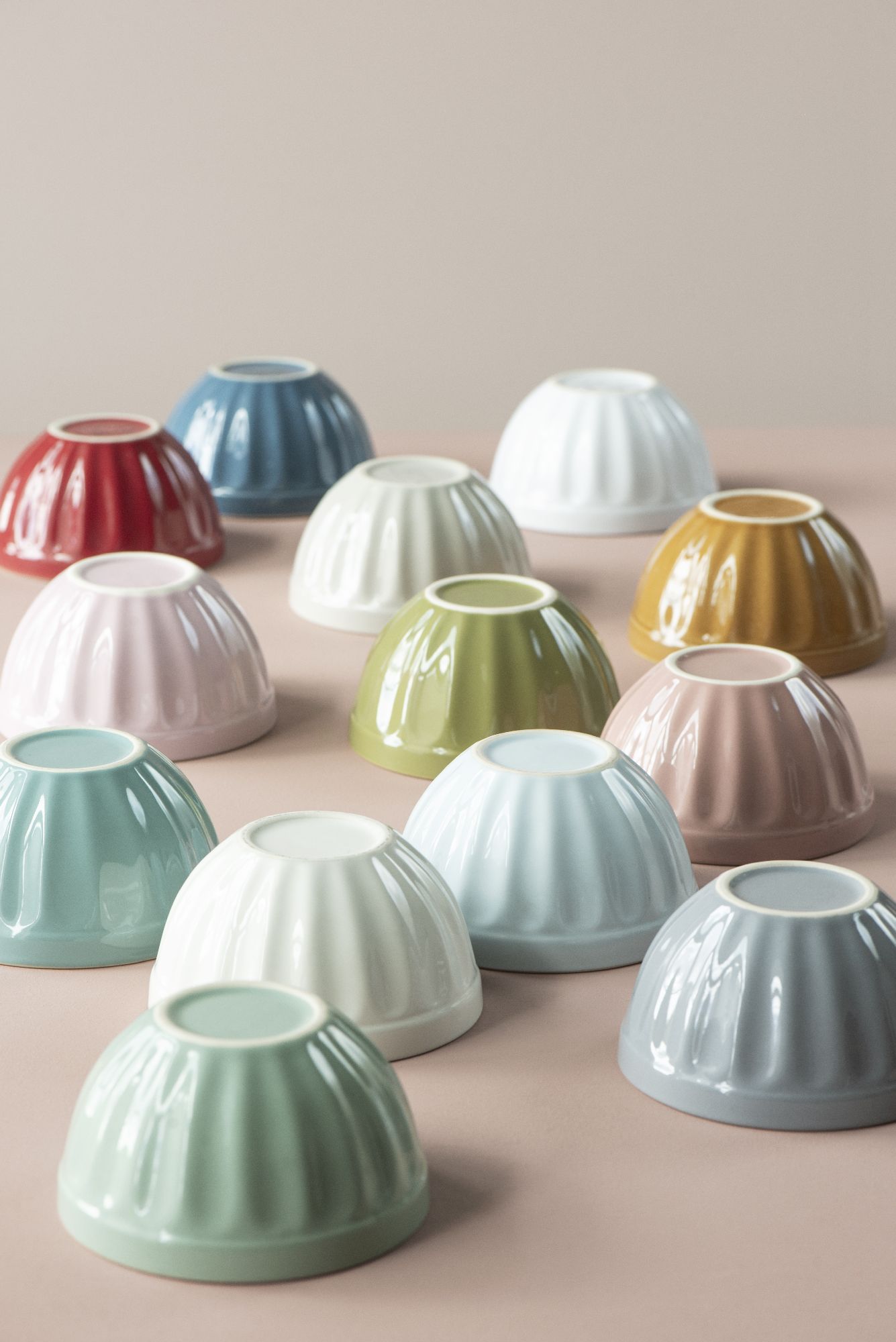 Bunte, runde Schalen in verschiedenen Farben stehen auf einer neutralen Unterlage. Die Schalen haben eine gewellte Oberfläche.