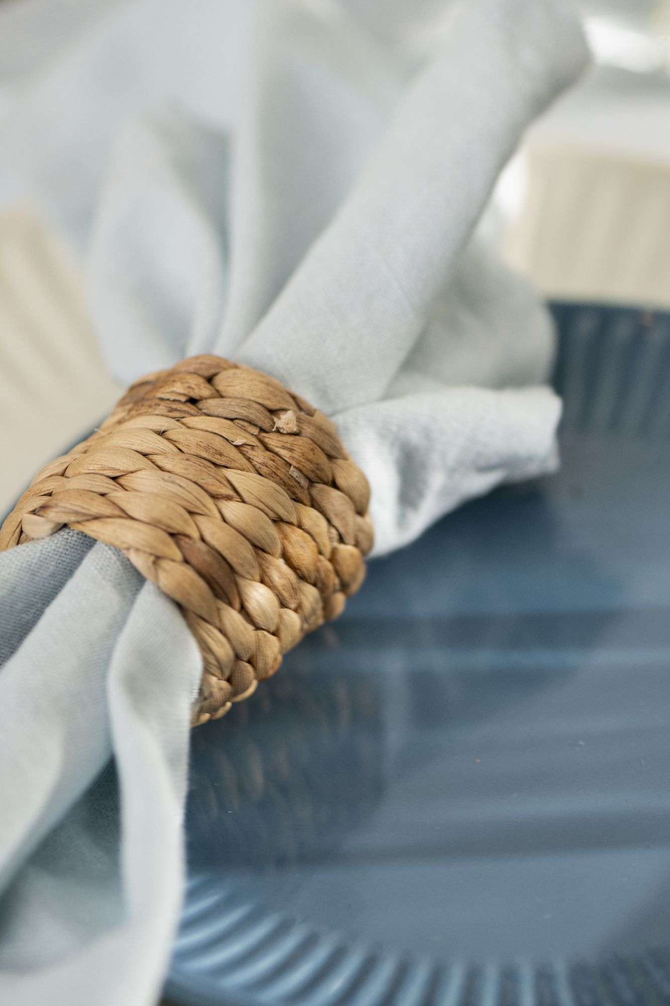 Ein blauer Teller mit einer gefalteten Serviette, die von einem geflochtenen Ring aus Naturmaterial gehalten wird.
