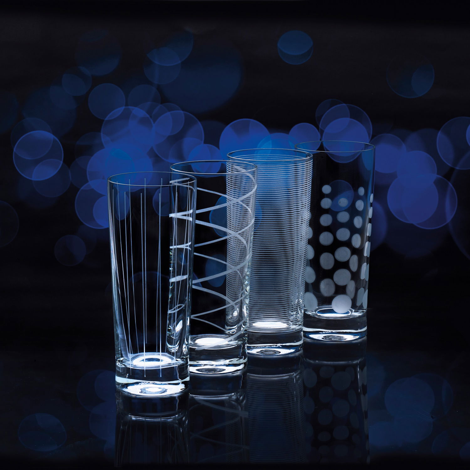 Vier verschiedene Gläser mit unterschiedlichen Mustern stehen vor einem unscharfen, blauen Hintergrund.