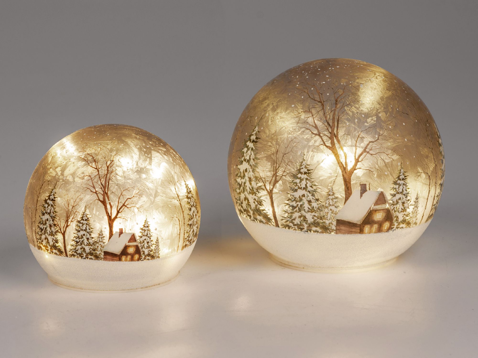 Zwei gläserne Kugeln mit winterlicher Landschaft, Bäumen und einem kleinen Haus, beleuchtet von inne