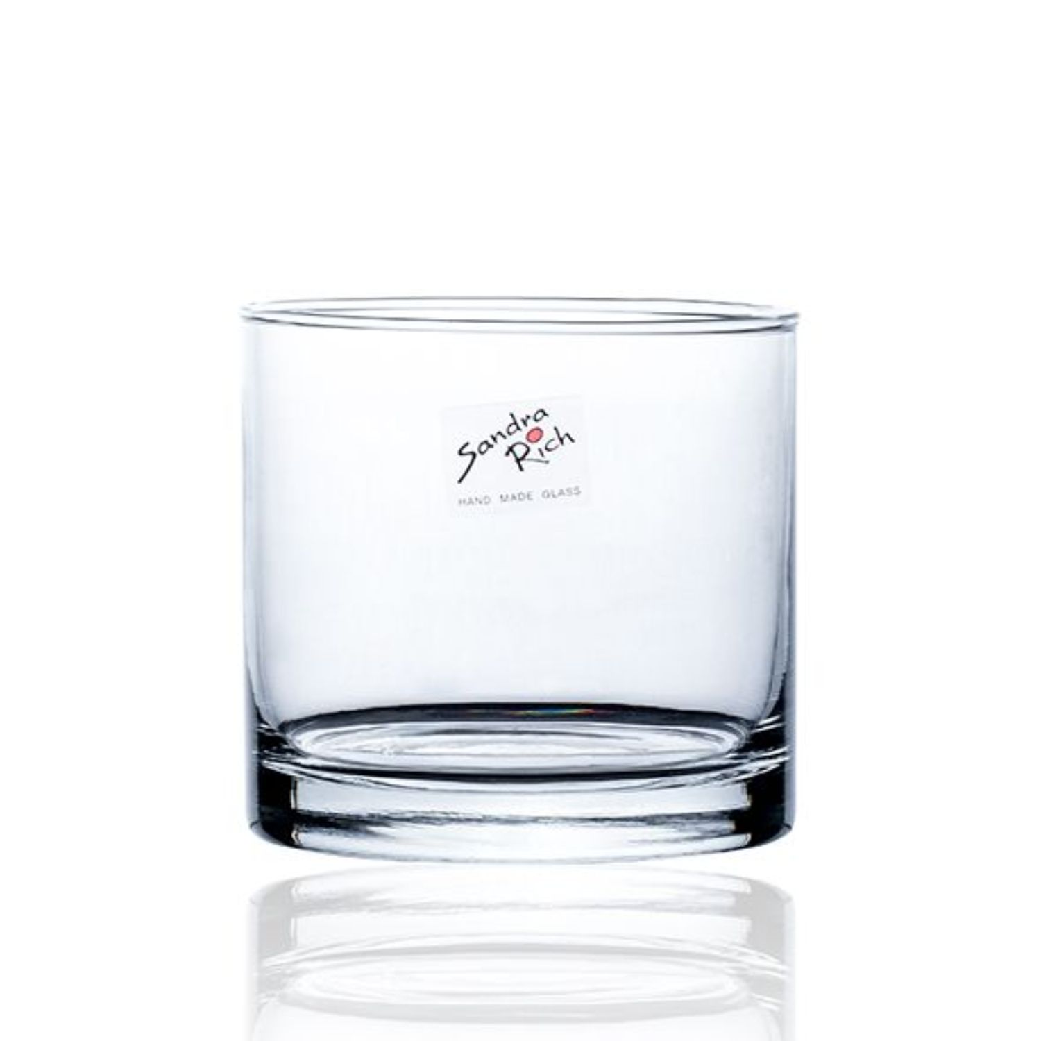 Ein transparenter Glasbehälter steht auf einer weißen Oberfläche, daneben ein weiteres Glas mit Wasser und Blumen.