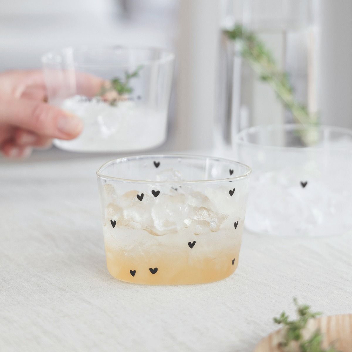 Ein Glas mit Eis und einem Getränk steht auf einem Tisch. Eine Hand hält ein weiteres Glas mit Eis.