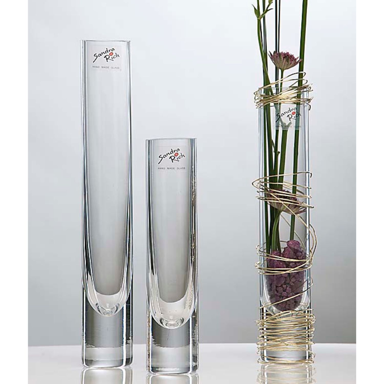 Drei schlanke Glasvasen, rechts mit Blumen und goldener Drahtspirale dekoriert