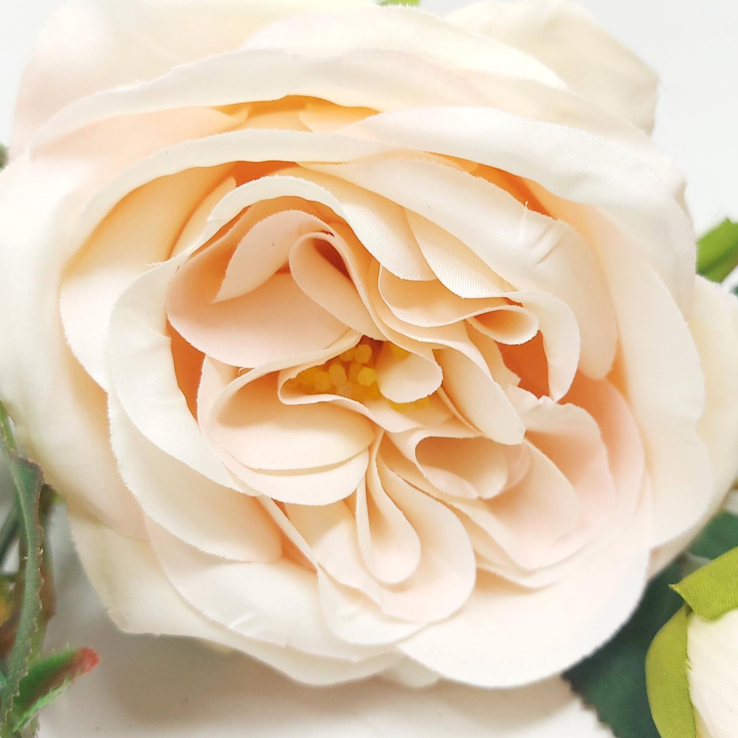 Eine zarte, künstliche Blume in sanften Rosatönen mit geschichteten Blütenblättern und gelben Staubgefäßen in der Mitte.