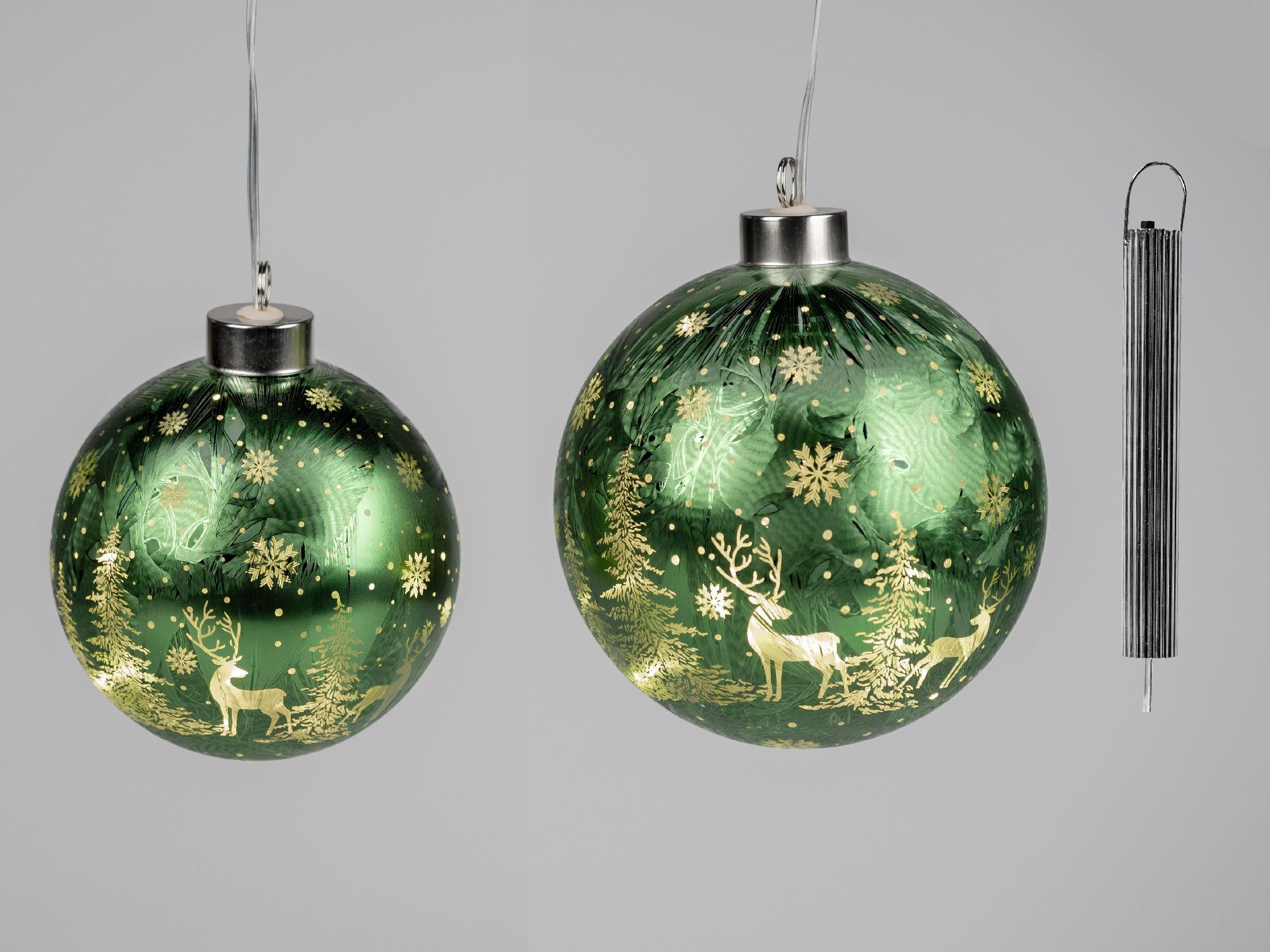 Zwei grüne Weihnachtskugeln mit goldenen Motiven von Rehen und Schneeflocken, daneben ein silberner