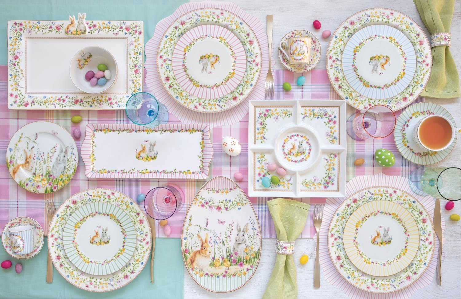 Tischgedeck mit buntem Geschirr, Gläsern und Besteck auf einem karierten Tischcloth. Bunte Schokoladeneier sind verteilt.