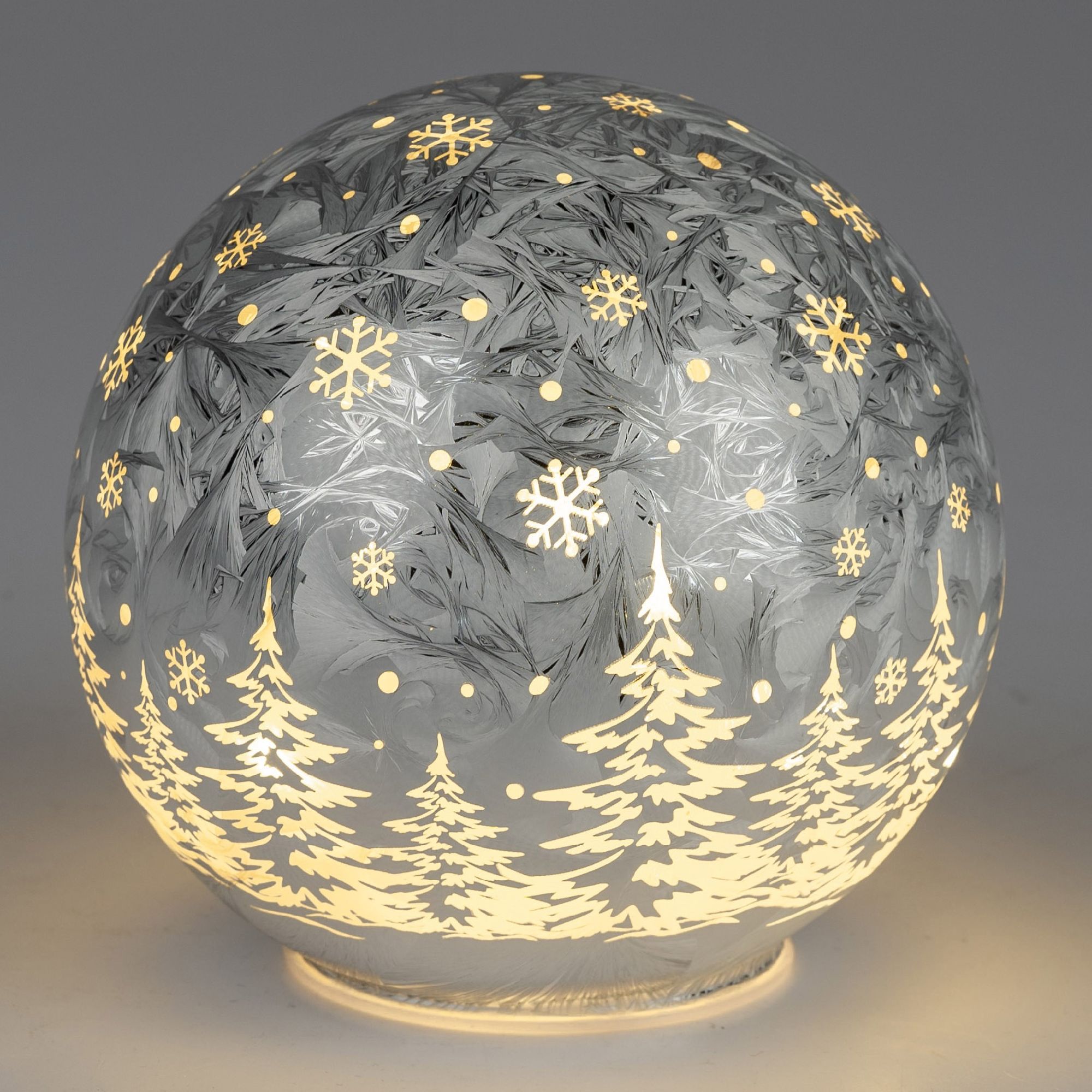 Eine runde, beleuchtete Weihnachtskugel mit frostigem Design, Schneeflocken und Tannenbäumen in hell