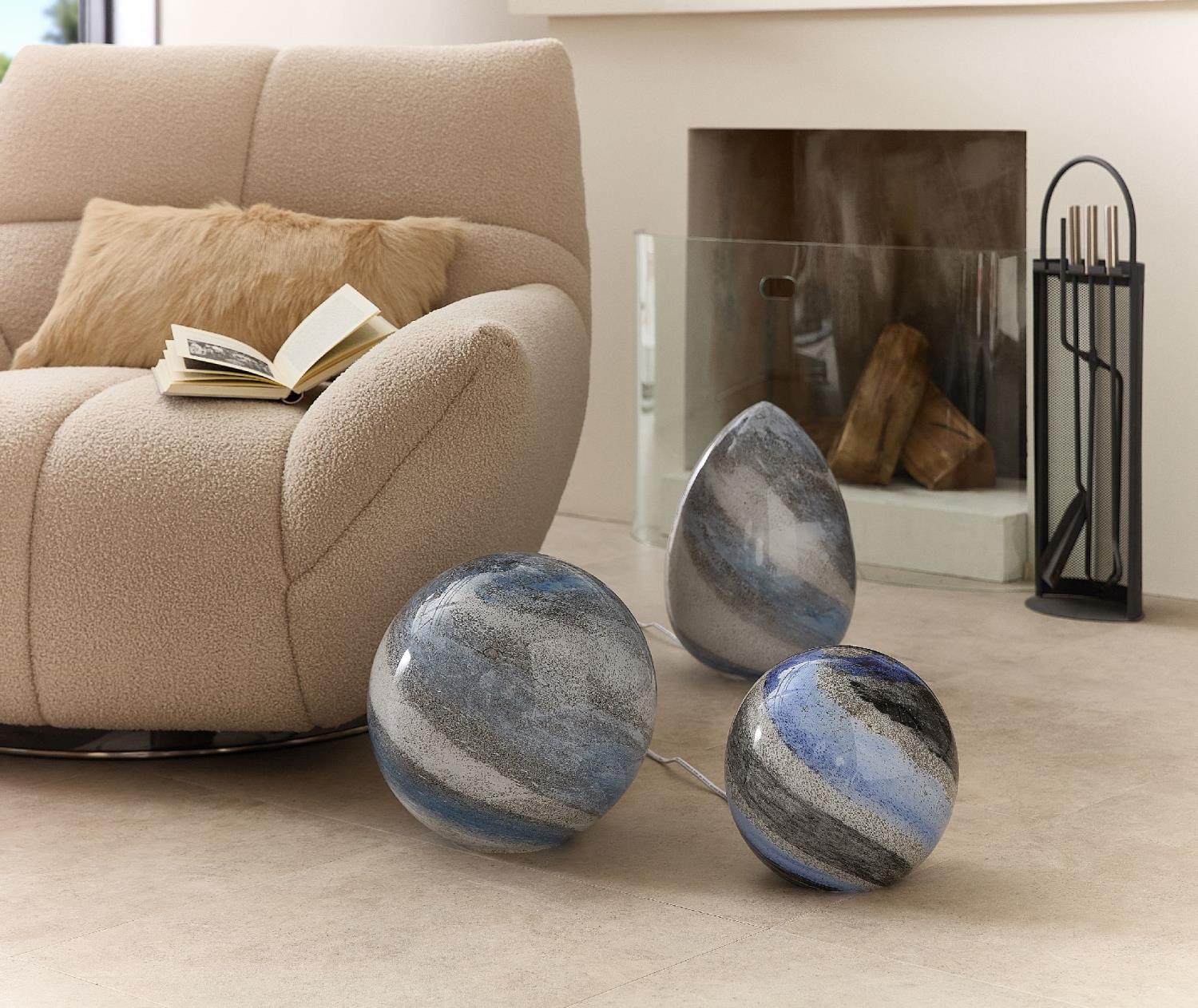 Beige Couch mit einem Kissen und einem offenen Buch. Drei dekorative Objekte in Blau- und Grautönen liegen auf dem Boden.