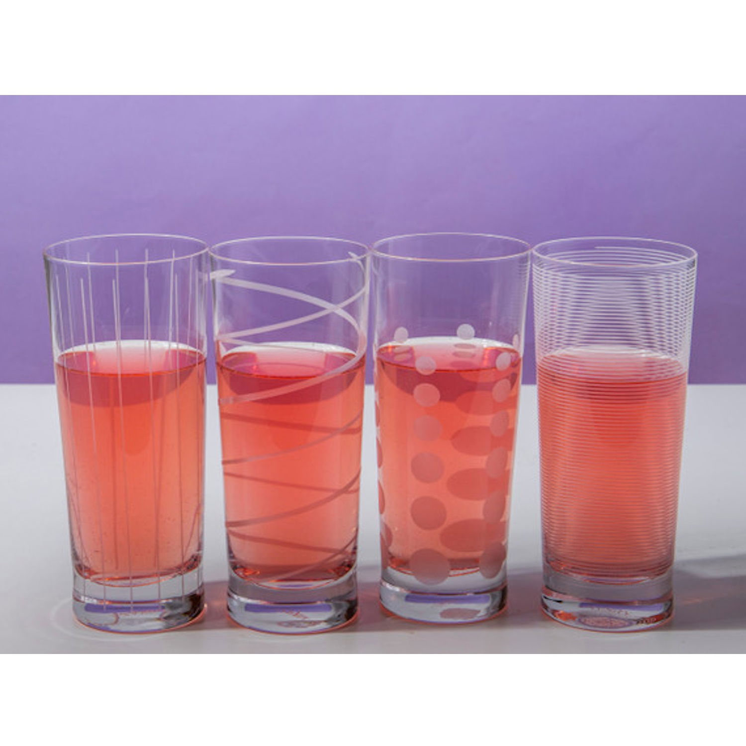 Vier Gläser mit rotem Getränk stehen nebeneinander. Jedes Glas hat ein unterschiedliches Muster. Der Hintergrund ist lila.
