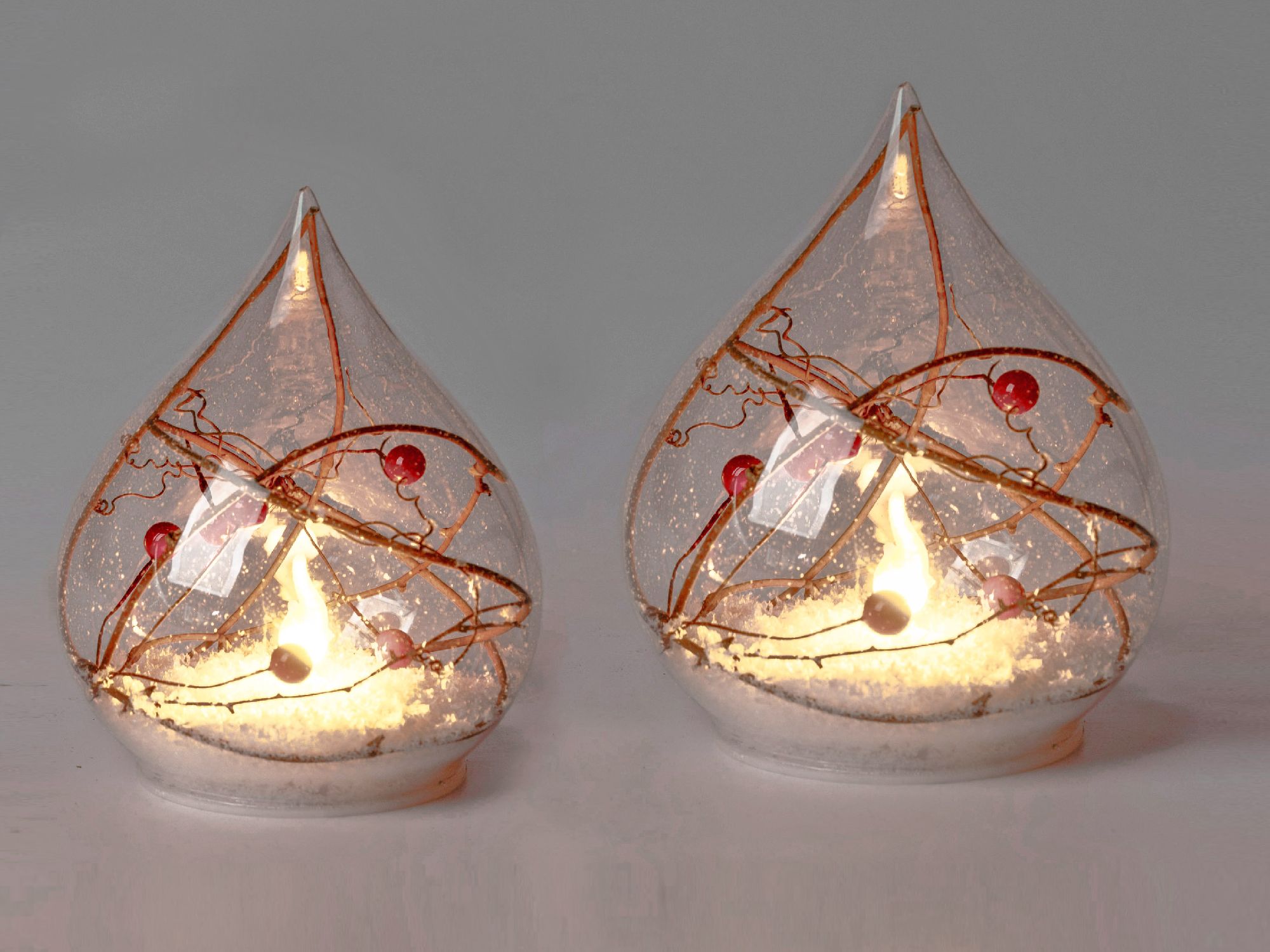 Zwei gläserne Dekolampen in Tropfenform mit goldenen Fäden und roten Kugeln, die warmes Licht ausstr