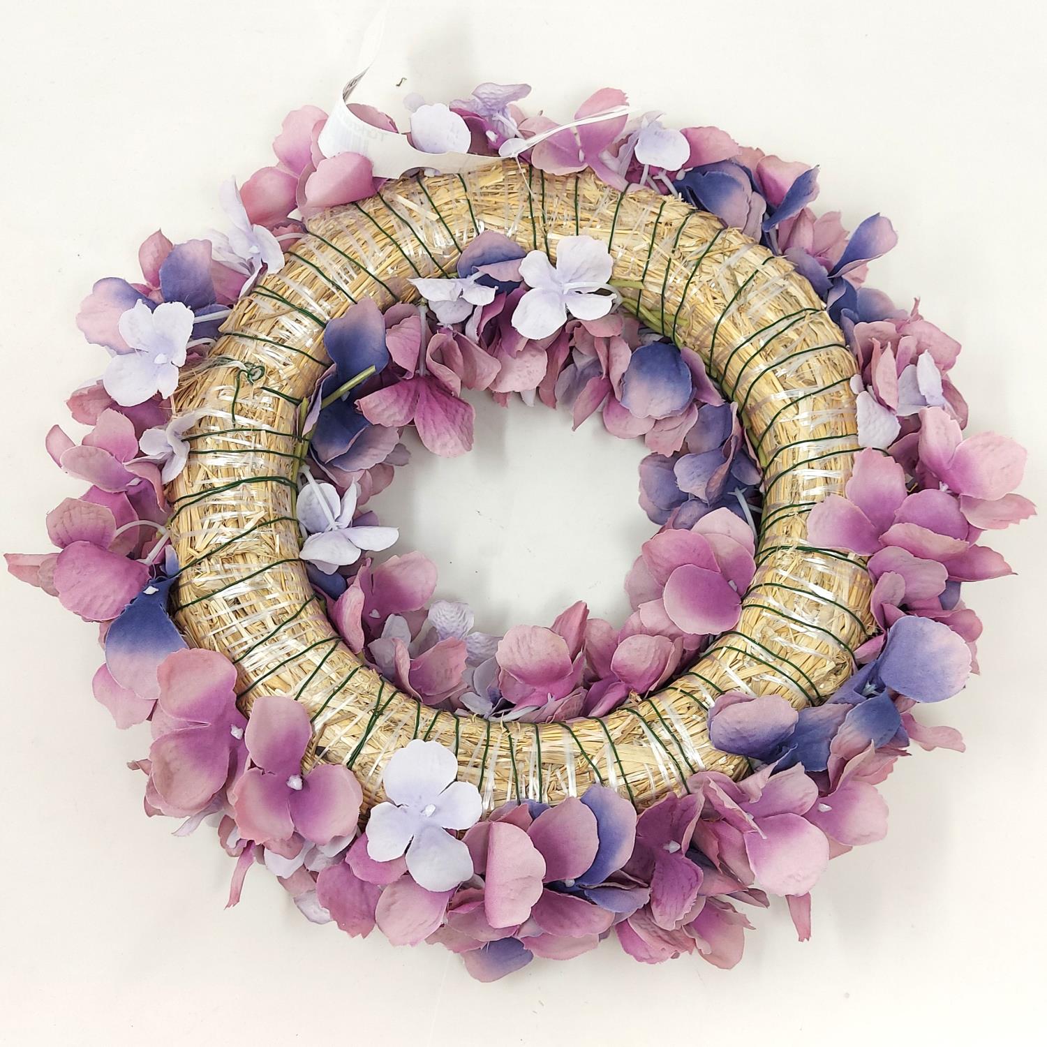 Ein runder Kranz aus Stroh, umgeben von lila und rosa Blütenblättern, mit kleinen weißen Blüten.