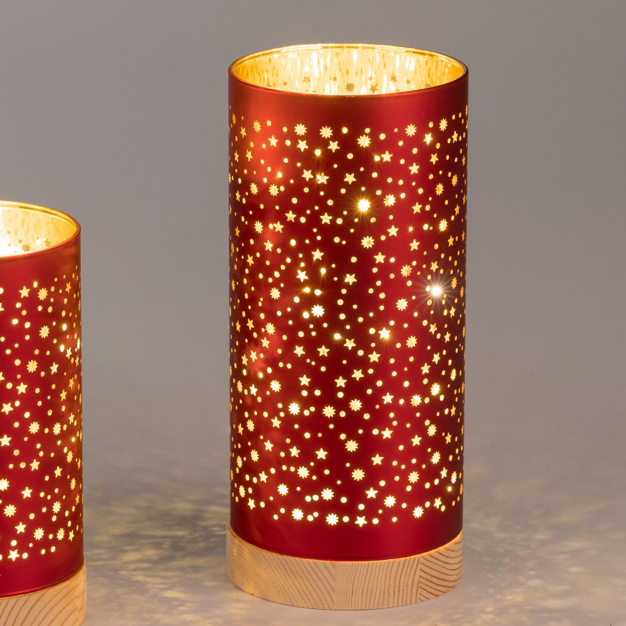 Zwei rote Laternen mit sternförmigen Ausschnitten, die warmes Licht ausstrahlen. Eine ist größer als