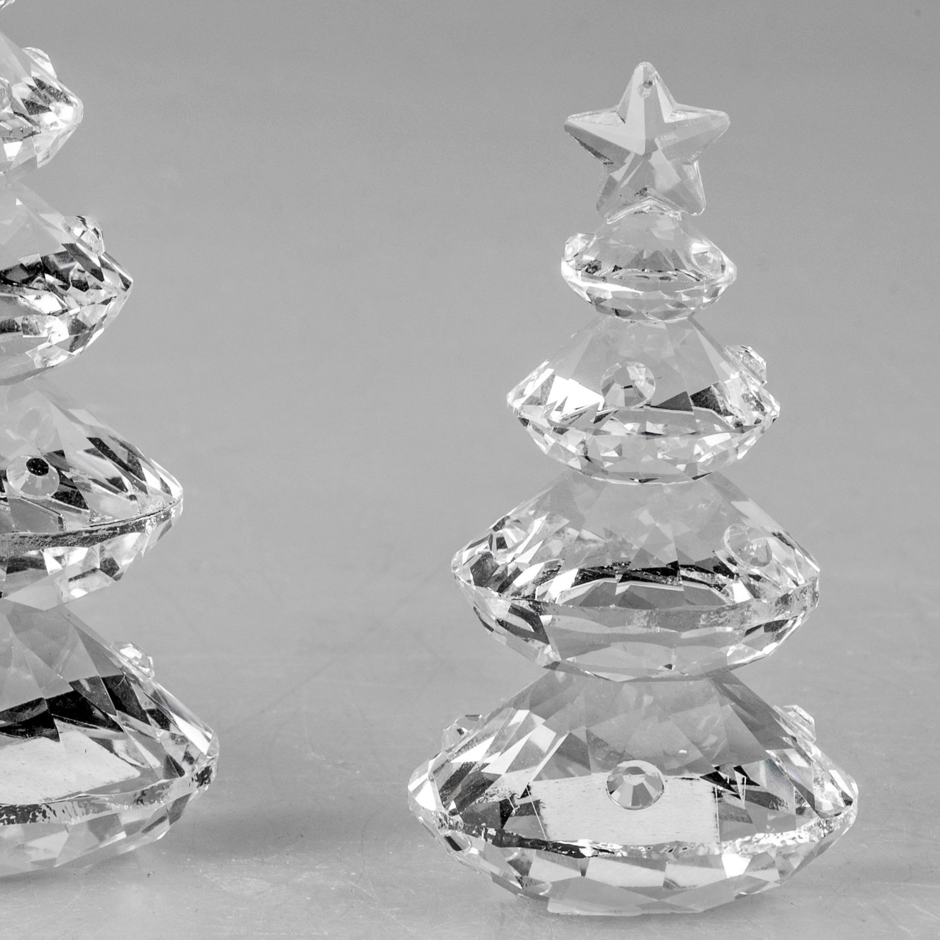 Zwei gläserne Weihnachtsbäume mit Sternen an der Spitze, auf einer grauen Oberfläche. Sie sind facet