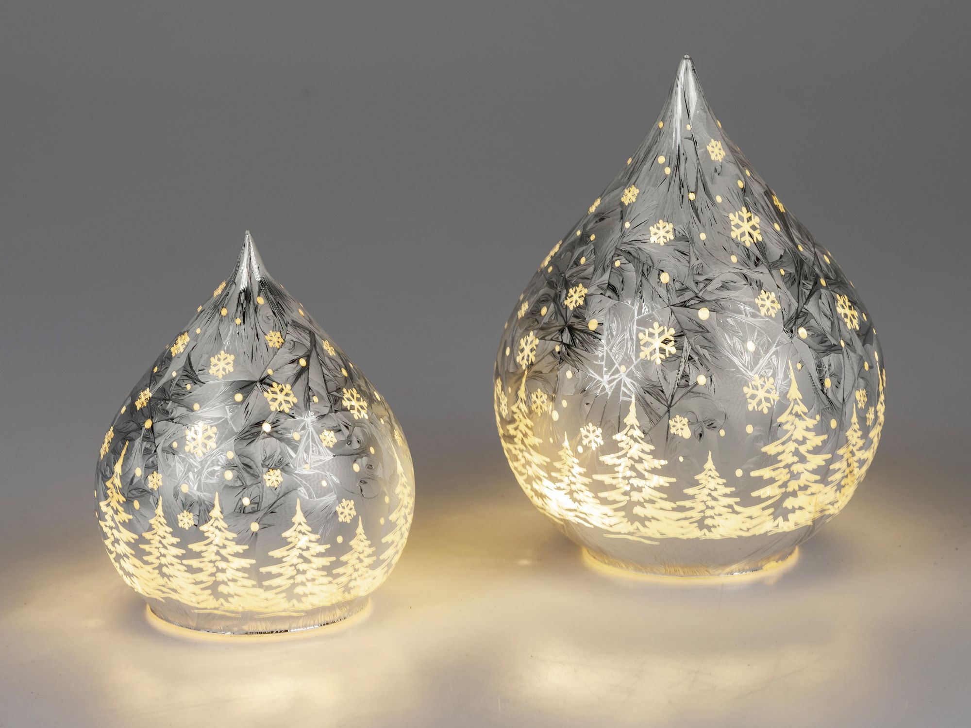 Zwei gläserne, tropfenförmige Objekte mit winterlichen Motiven, beleuchtet und in verschiedenen Größ