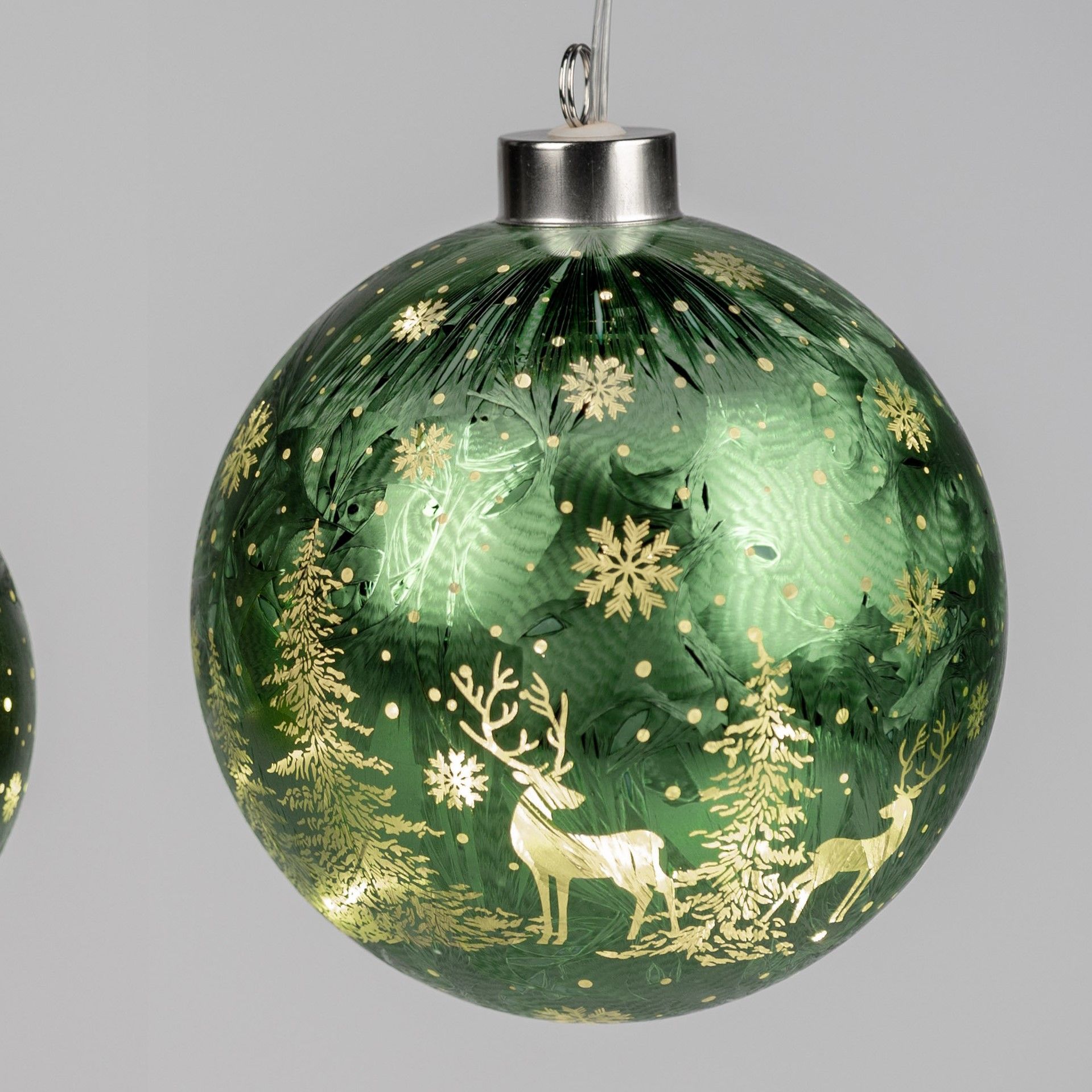 Grüne Weihnachtskugel mit goldenen Motiven von Bäumen, Schneeflocken und Rehen auf einer glatten Obe