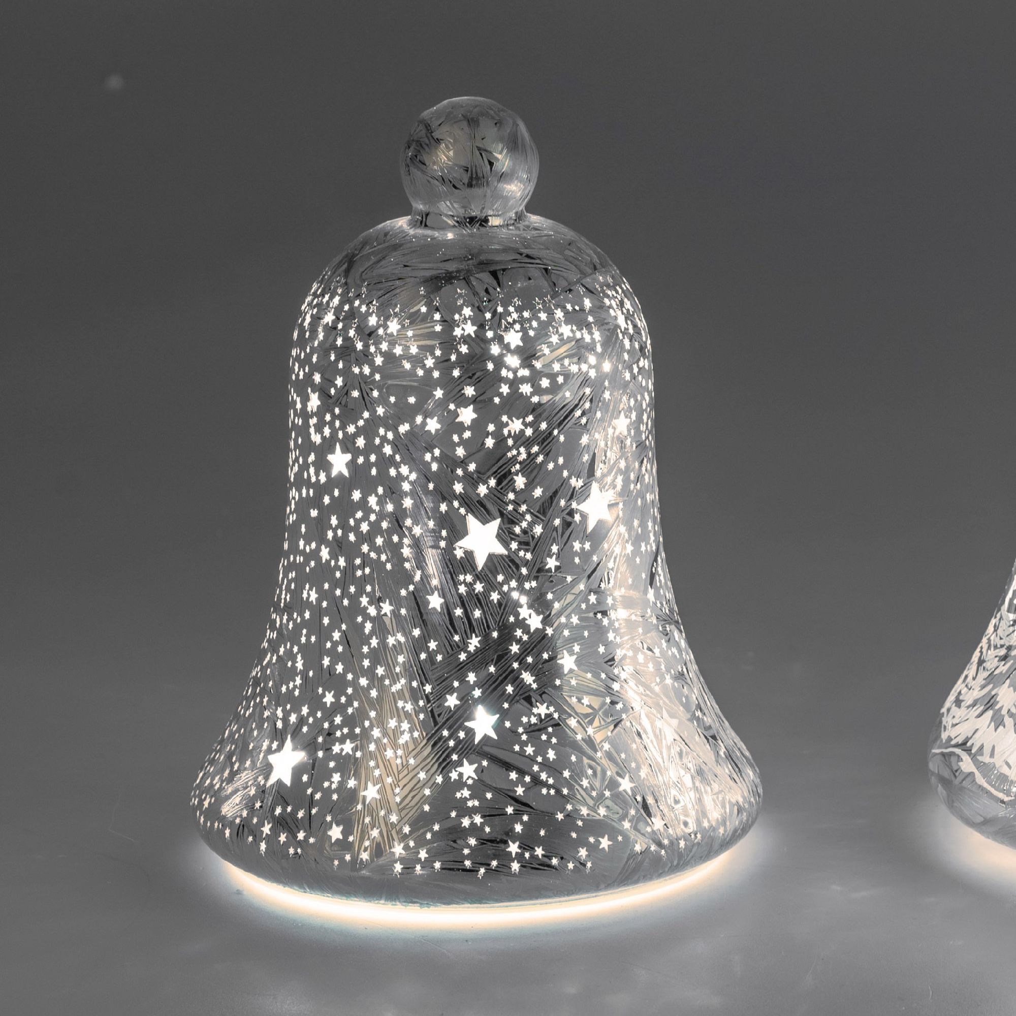 Glasglocke mit Sternen-Muster, beleuchtet von innen, auf grauem Hintergrund. Die Glocke hat eine run