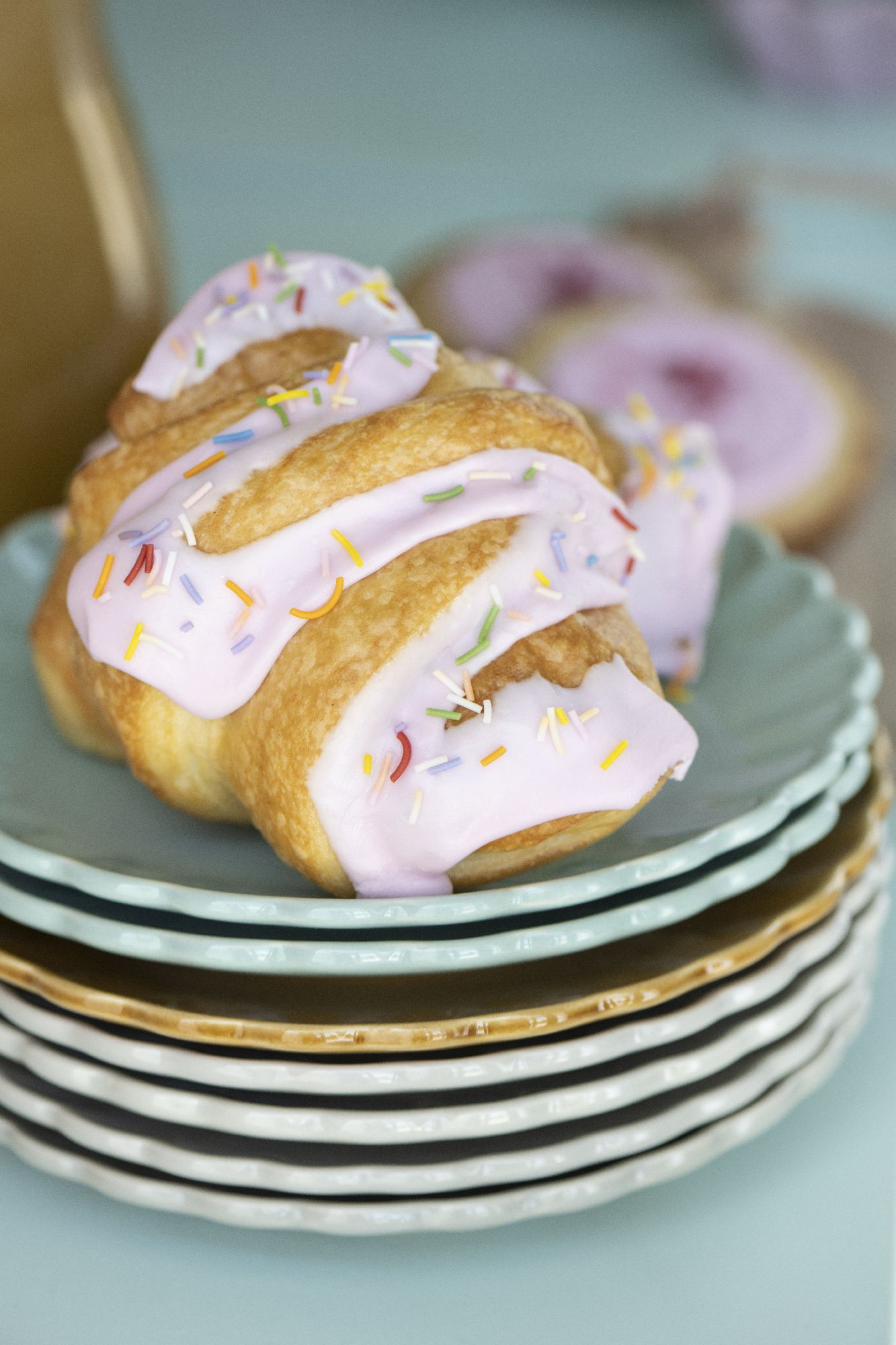 Ein gefülltes Gebäck mit rosa Zuckerguss und bunten Streuseln auf einem Stapel von Tellern.