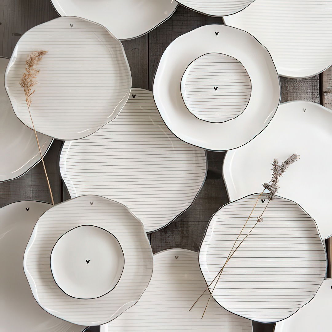 Mehrere Teller in verschiedenen Formen und Größen, mit feinen Linien und einem kleinen Zweig auf einem Teller, auf einem Holzuntergrund.