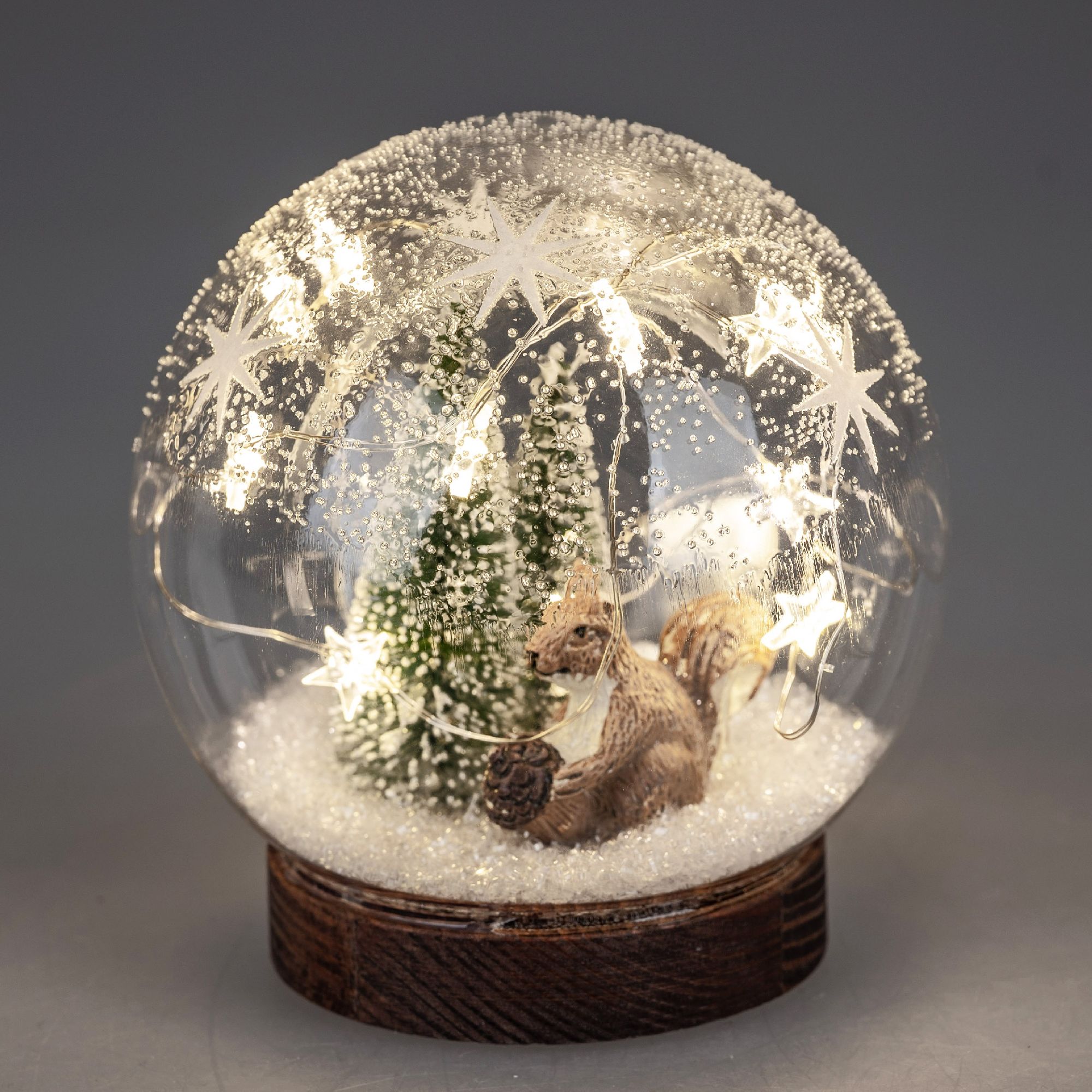 Eine Schneekugel mit einem Eichhörnchen, einem kleinen Baum und Lichtern, umgeben von Kunstschnee au