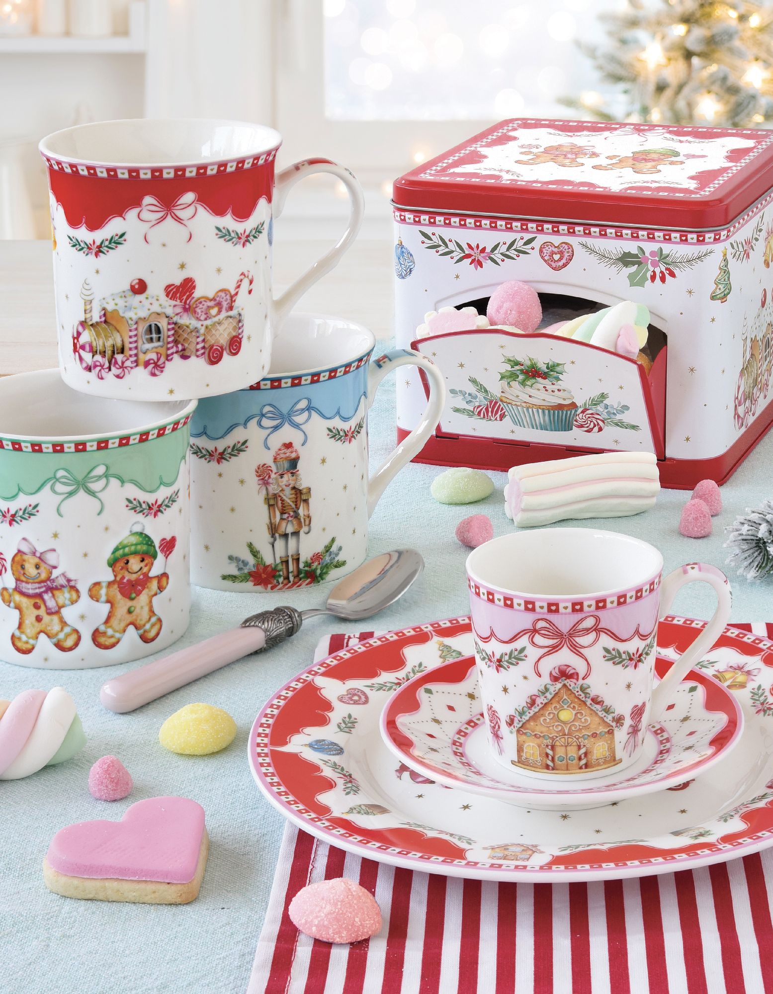 Bunte Tassen und Teller mit Weihnachtsmotiven auf einem Tisch mit Süßigkeiten